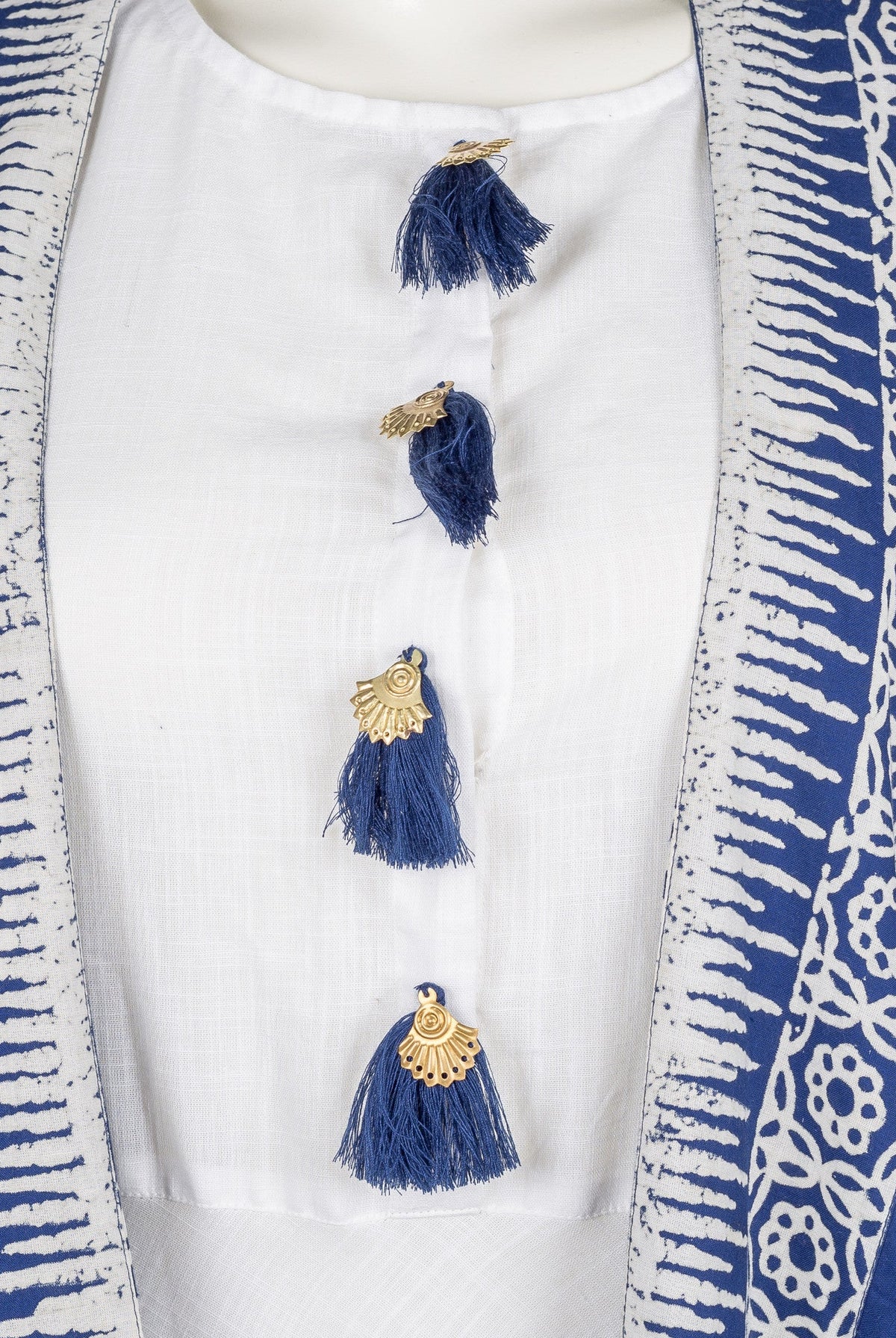Front close-up of white dress with blue tassels and blue-white block print shrug on mannequin.