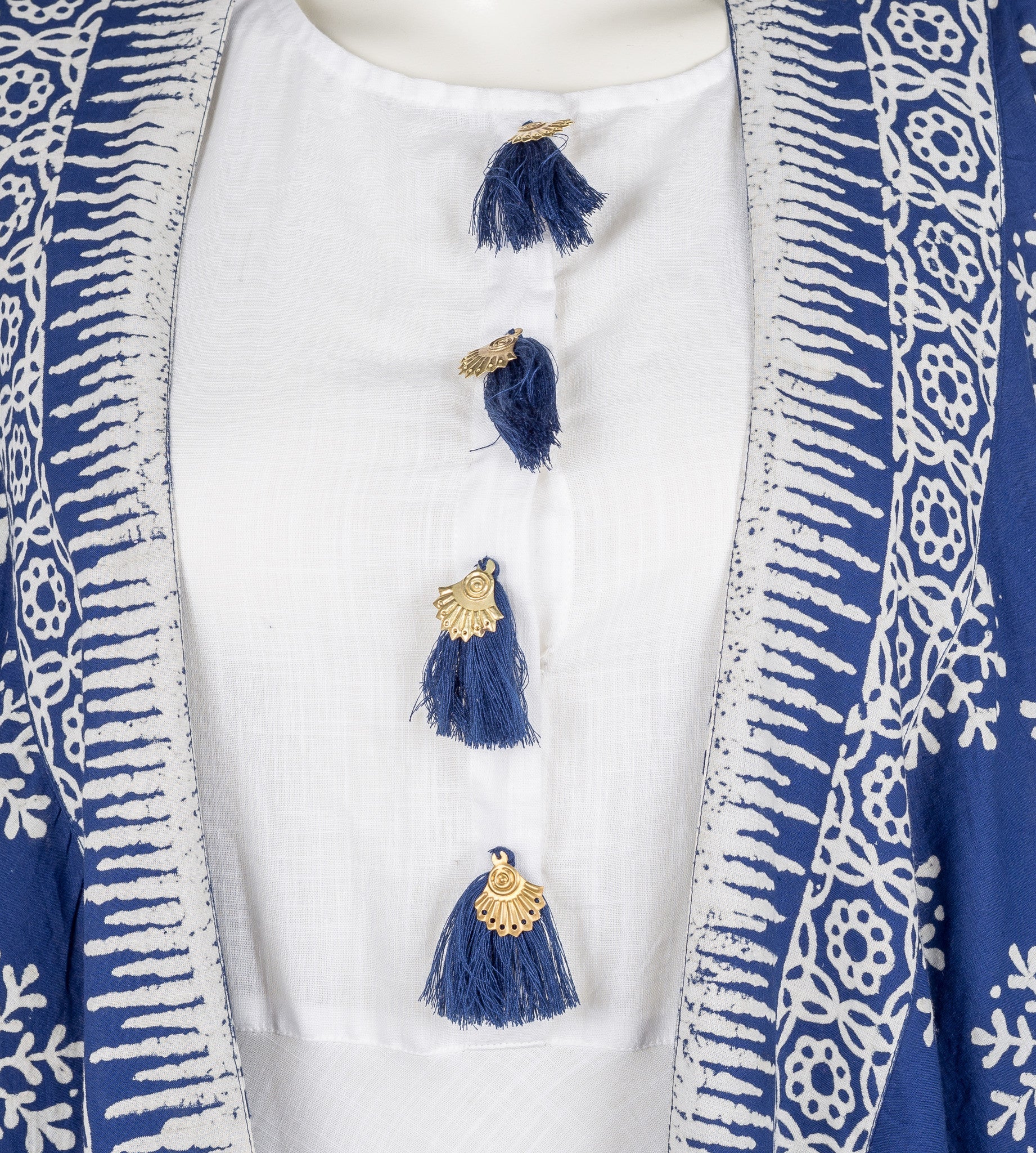 Front close-up of white dress with blue tassels and blue-white block print shrug on mannequin.