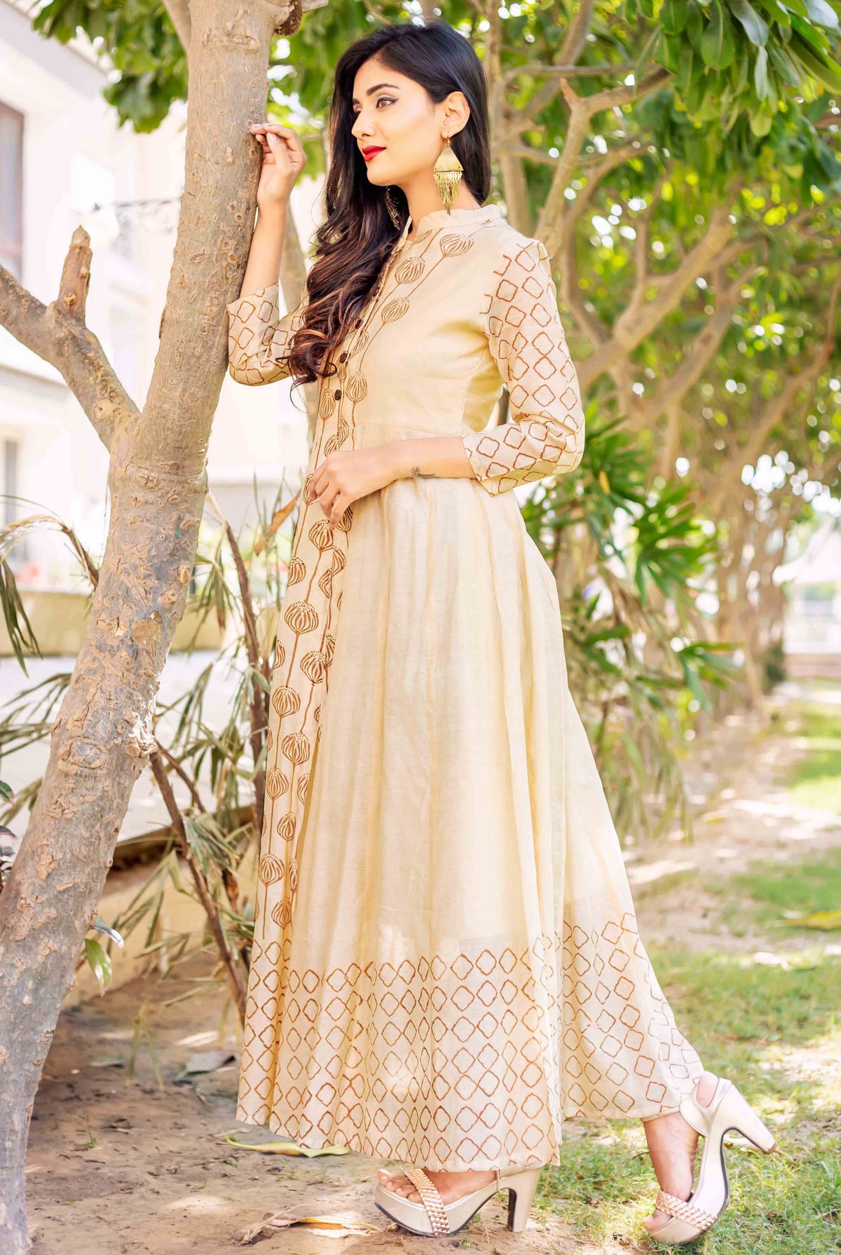 A model wearing a beige and brown printed dress, posing outdoors.