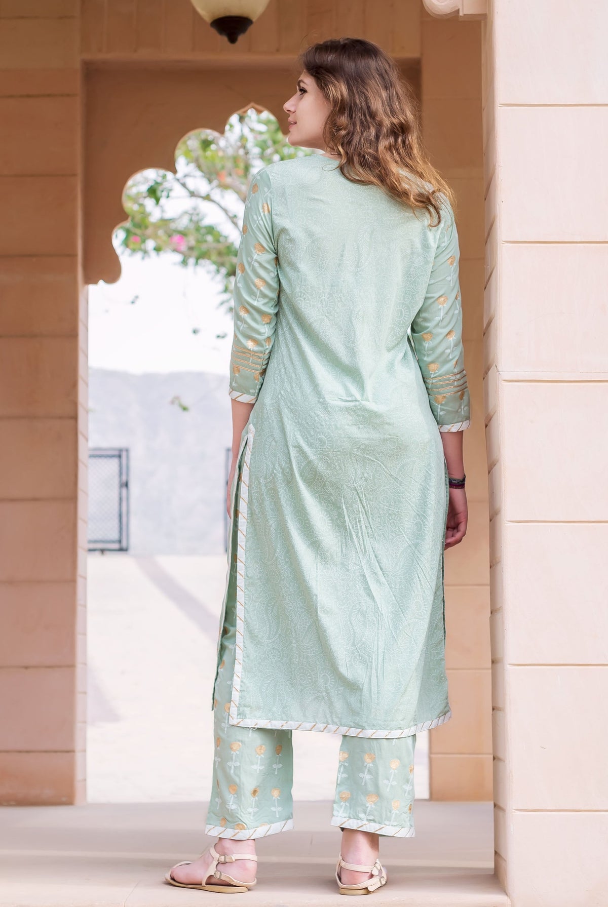 Back view of woman in mint green hand-block-printed cotton kurta set with gold motifs.