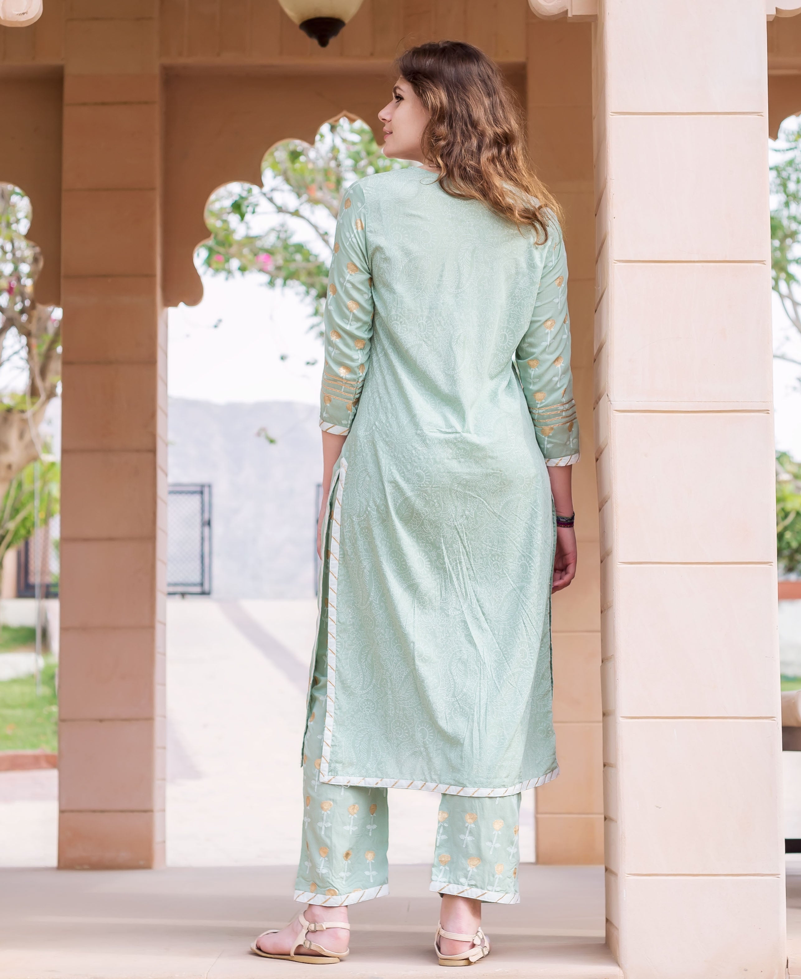 Back view of woman in mint green hand-block-printed cotton kurta set with gold motifs.