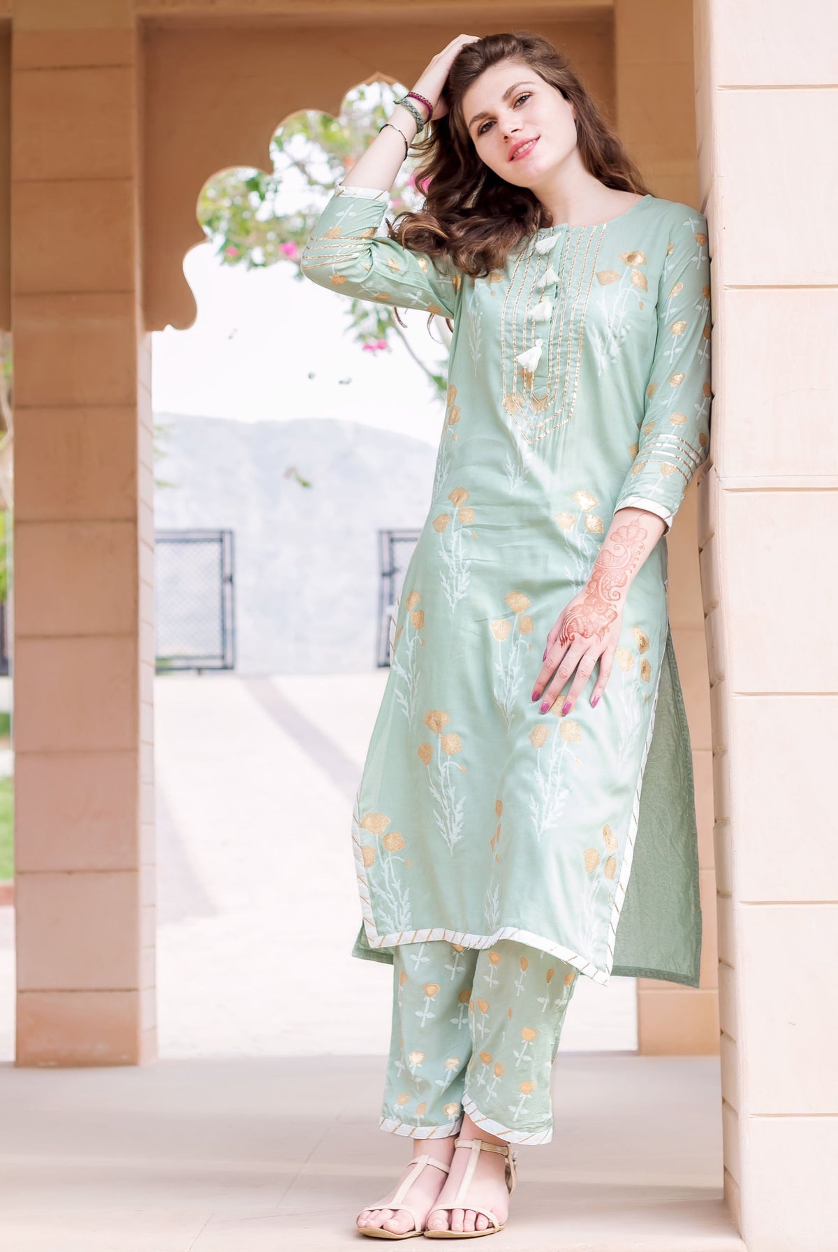 Model wearing a mint green kurta and pants set with gold floral print.