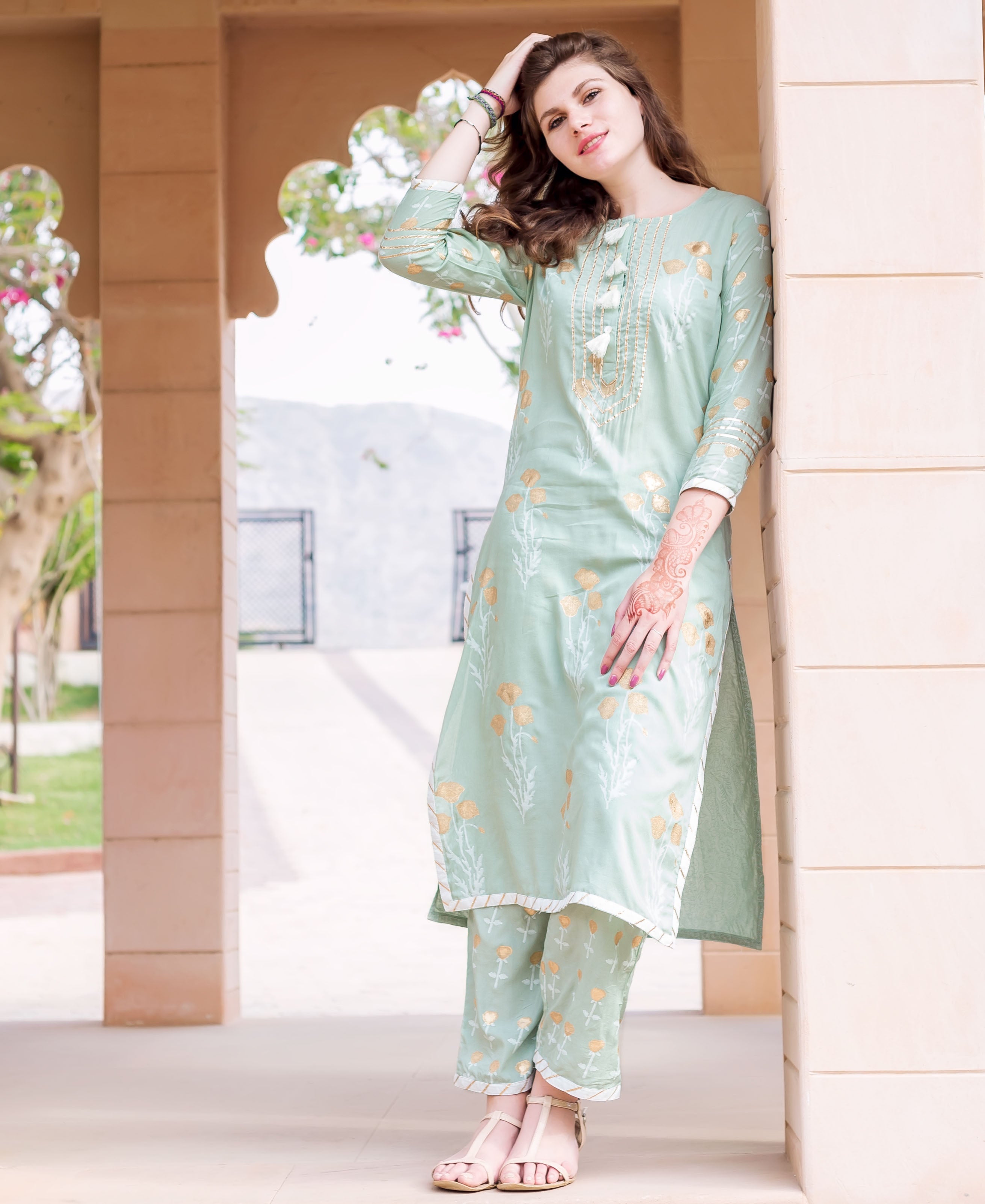 Model wearing a mint green kurta and pants set with gold floral print.