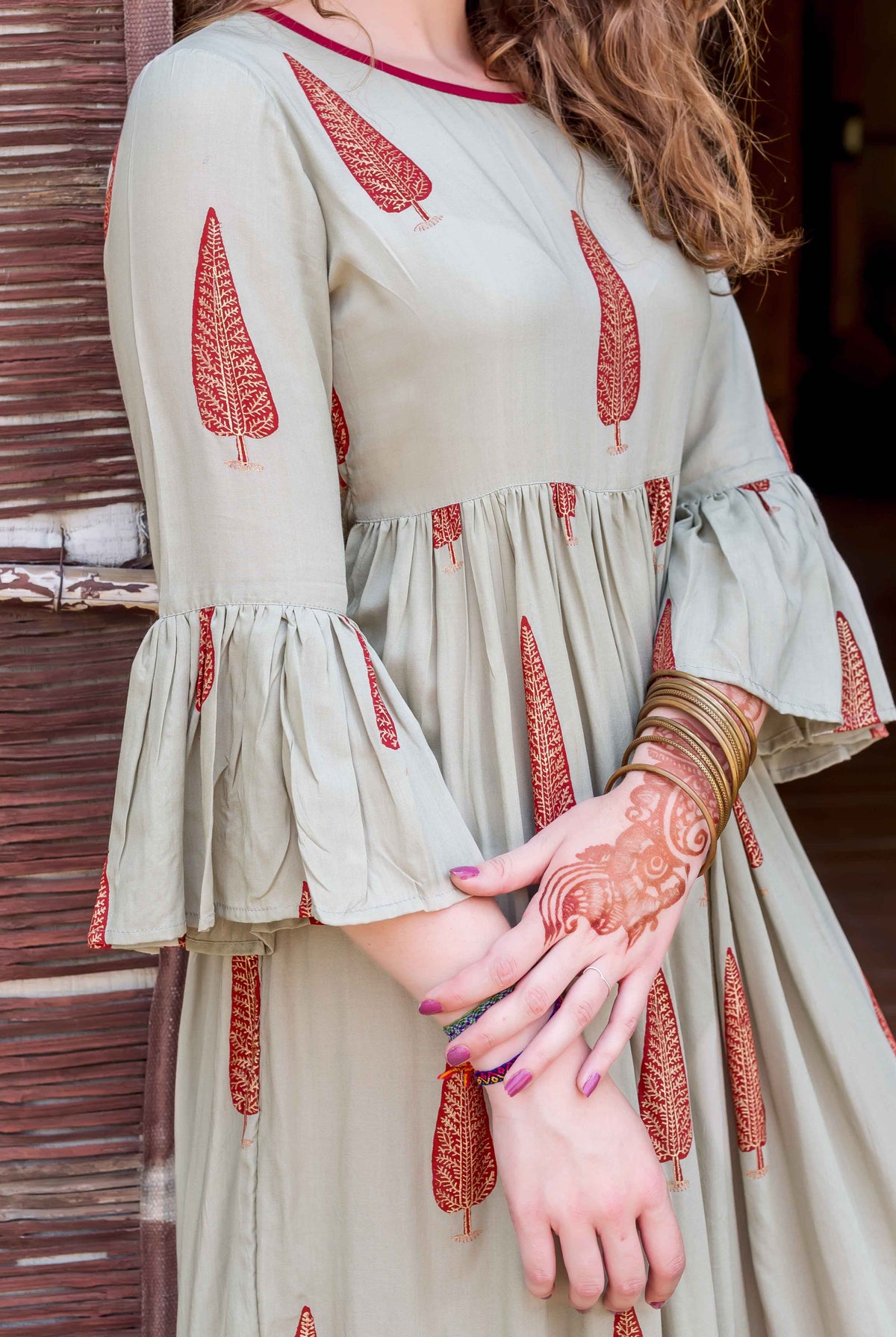 Sage green block-printed dress on model, featuring red tree patterns and gathered bell sleeves.