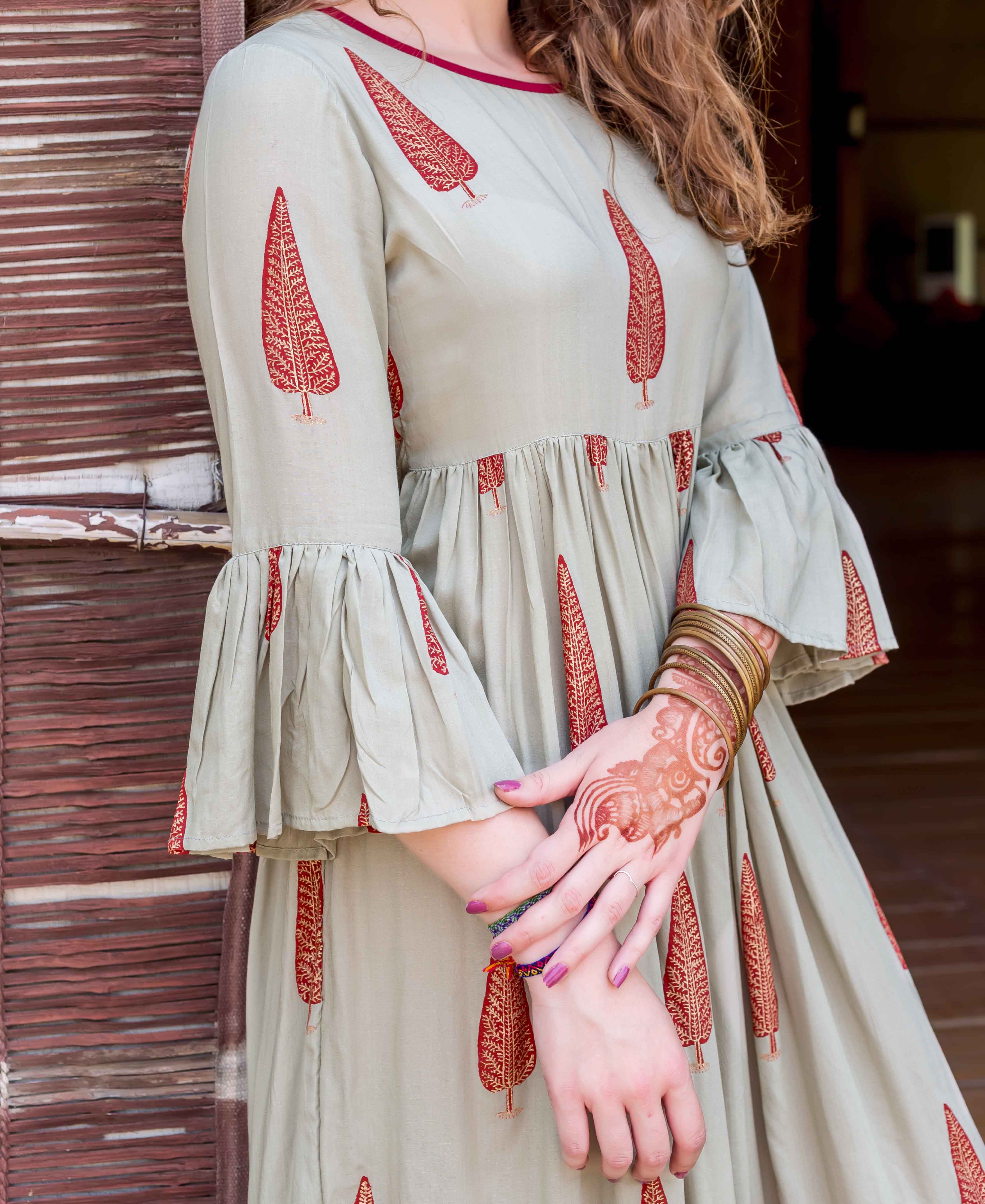 Sage green block-printed dress on model, featuring red tree patterns and gathered bell sleeves.