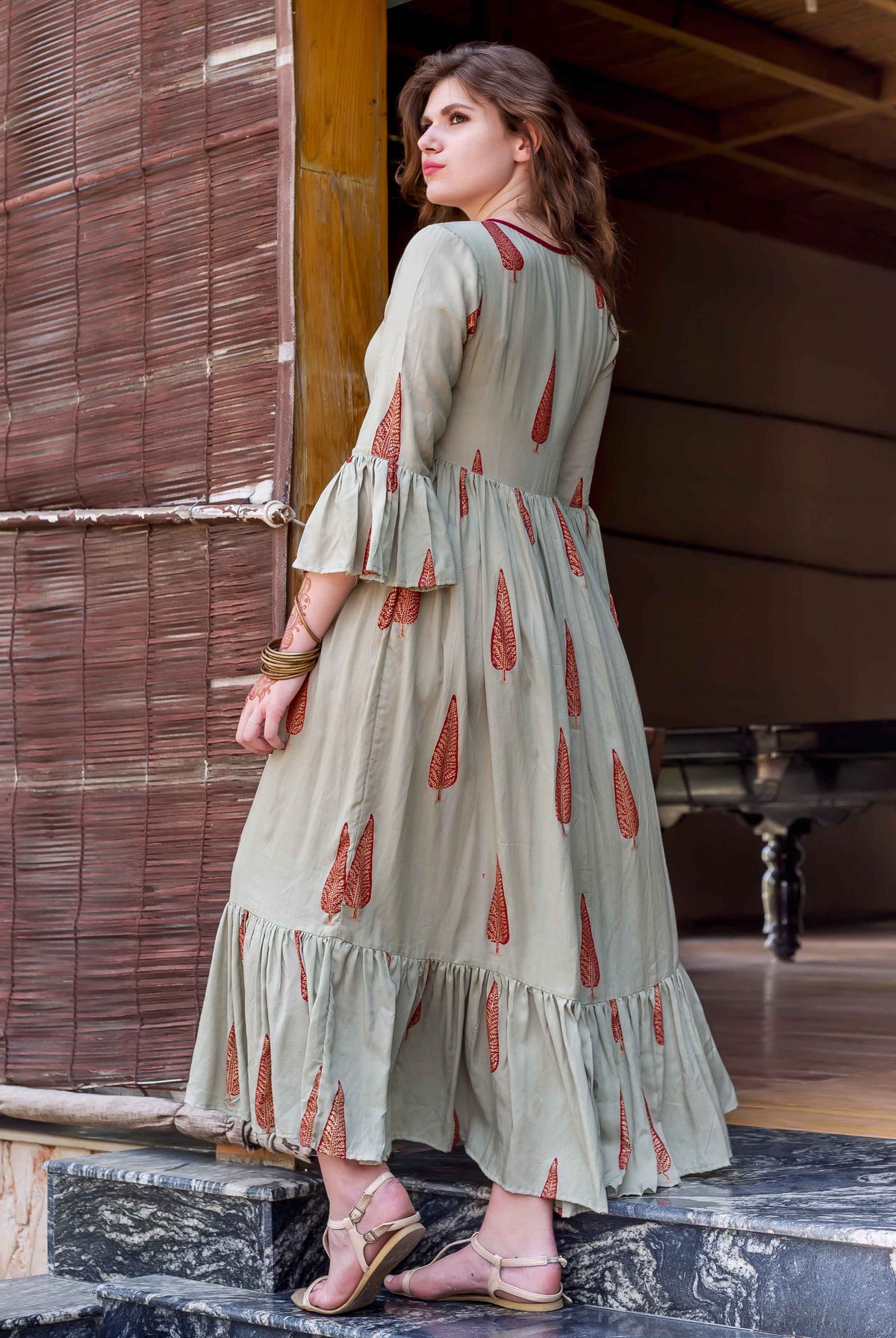 Model in sage green rayon block printed long dress with red leaf design and ruffles.