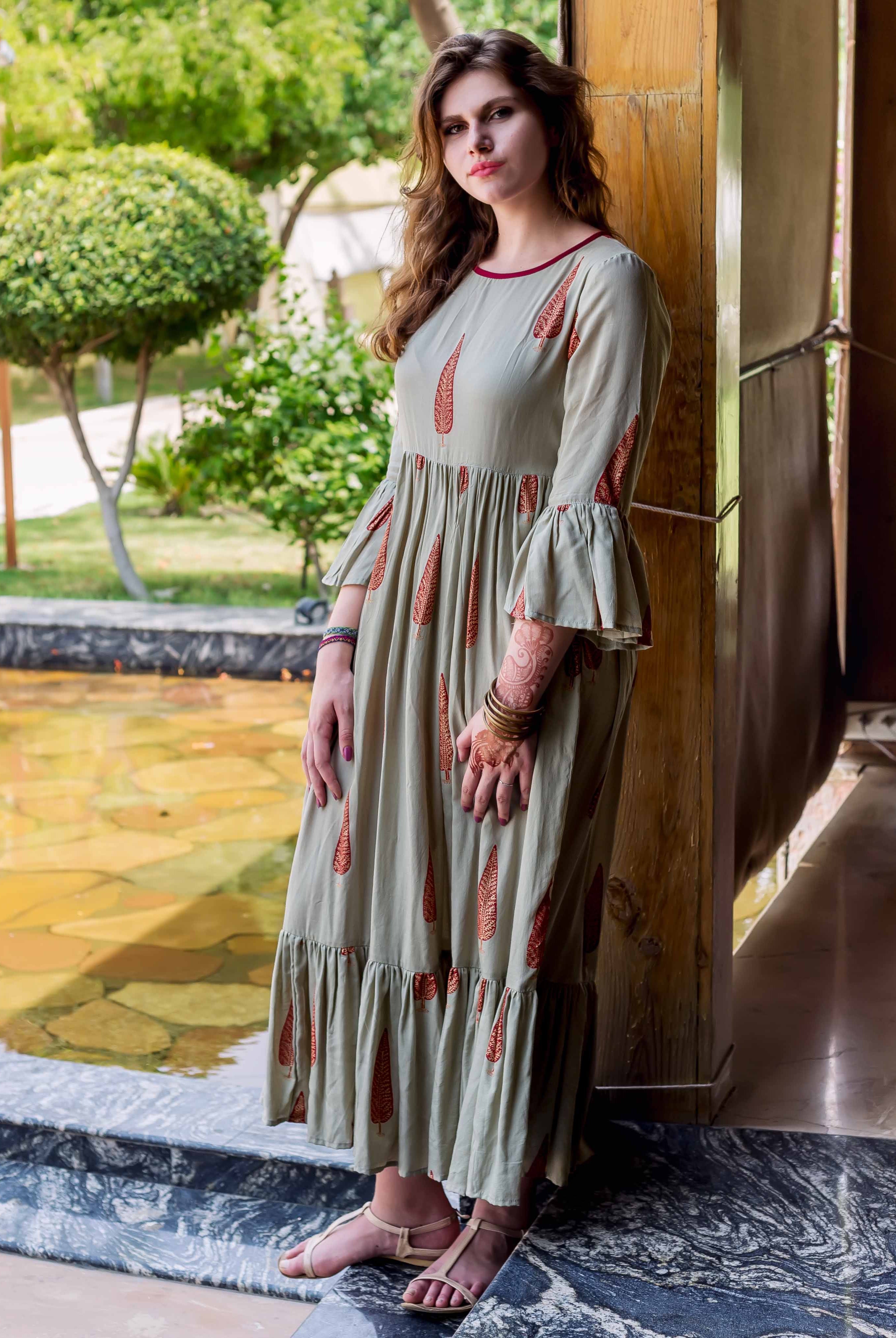 Model wearing a sage green long dress with red ethnic block print and bell sleeves.