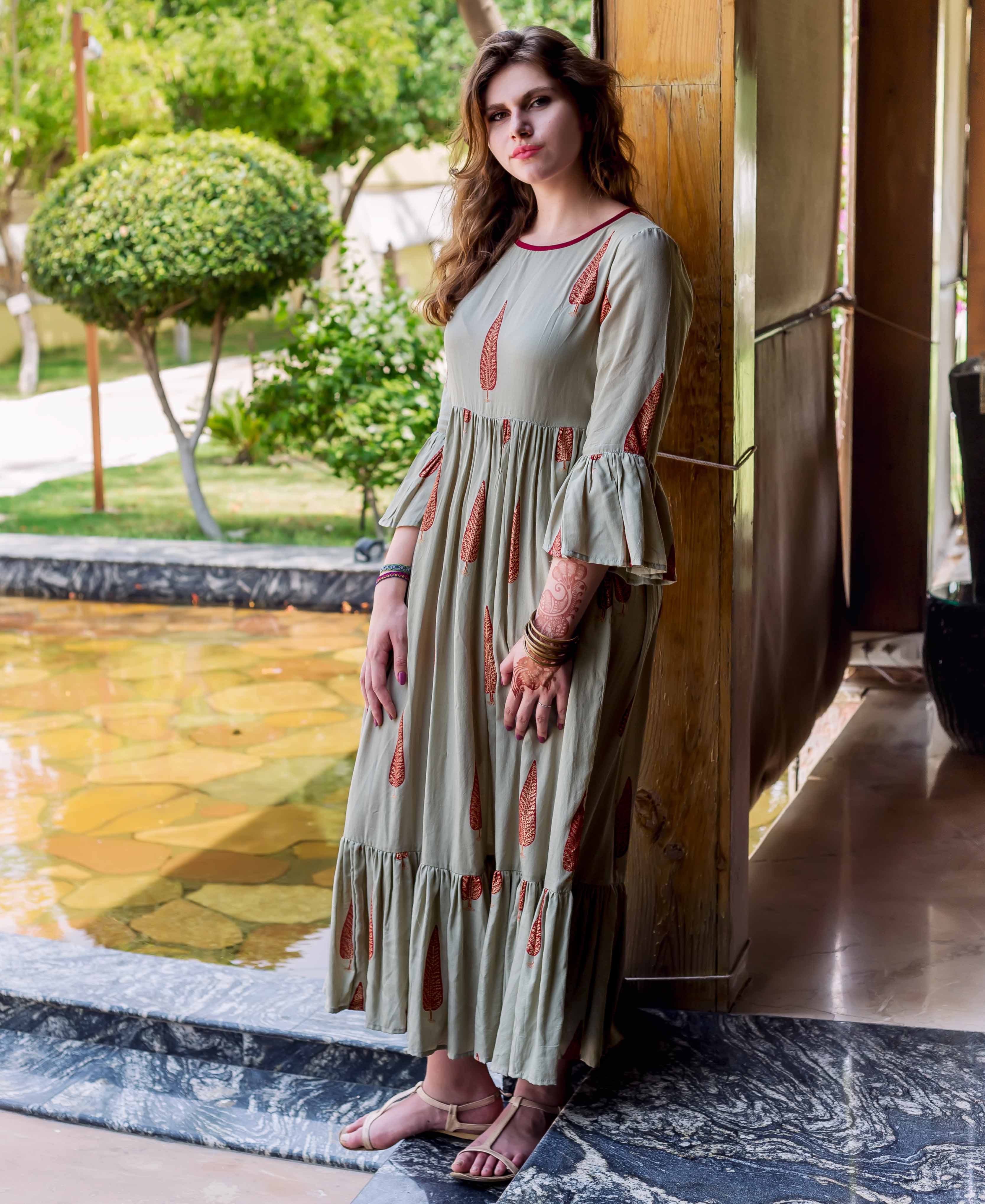 Model wearing a sage green long dress with red ethnic block print and bell sleeves.
