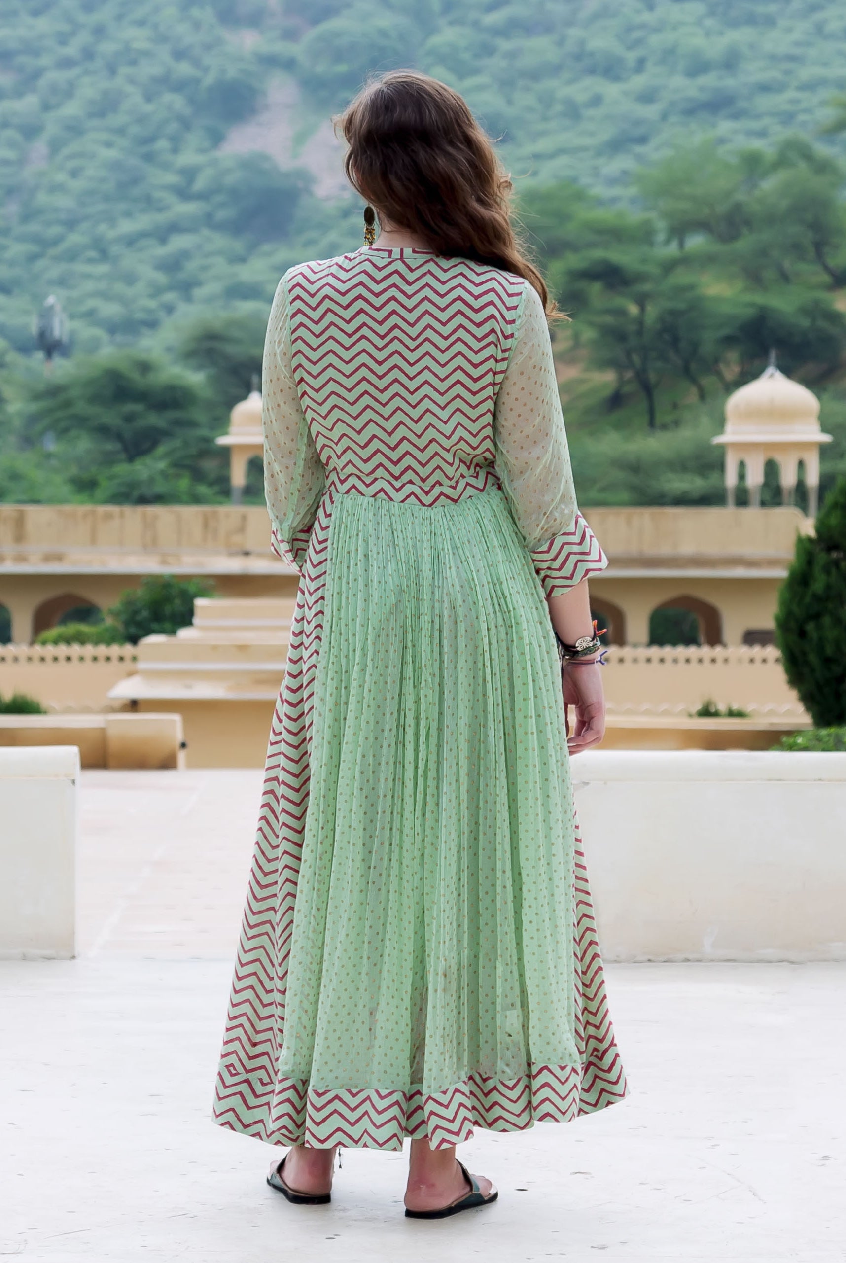 Back view of a model wearing a mint green Anarkali dress with red chevron and polka dot prints.