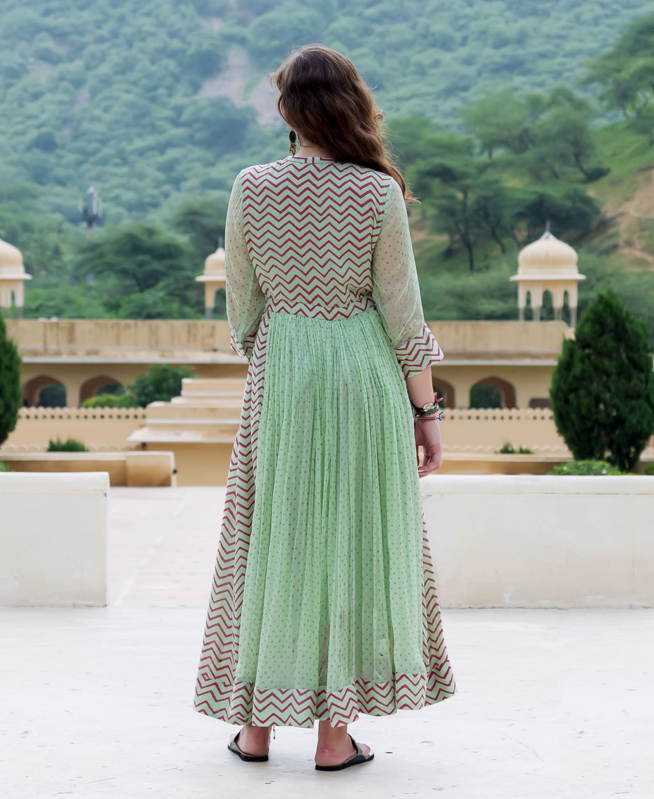 Back view of a model wearing a mint green Anarkali dress with red chevron and polka dot prints.