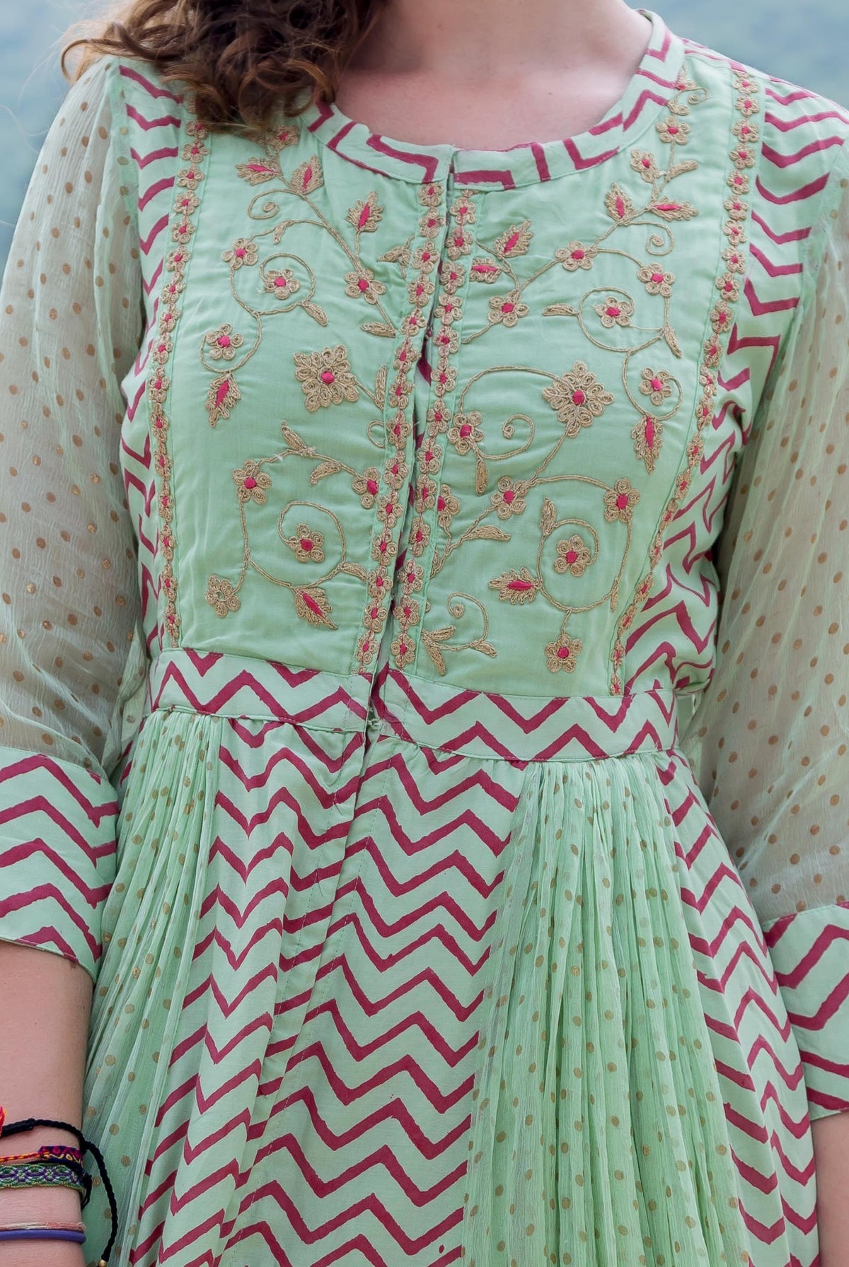 Mint green Anarkali dress with pink floral embroidery, zigzag pattern, and sheer polka dot sleeves.