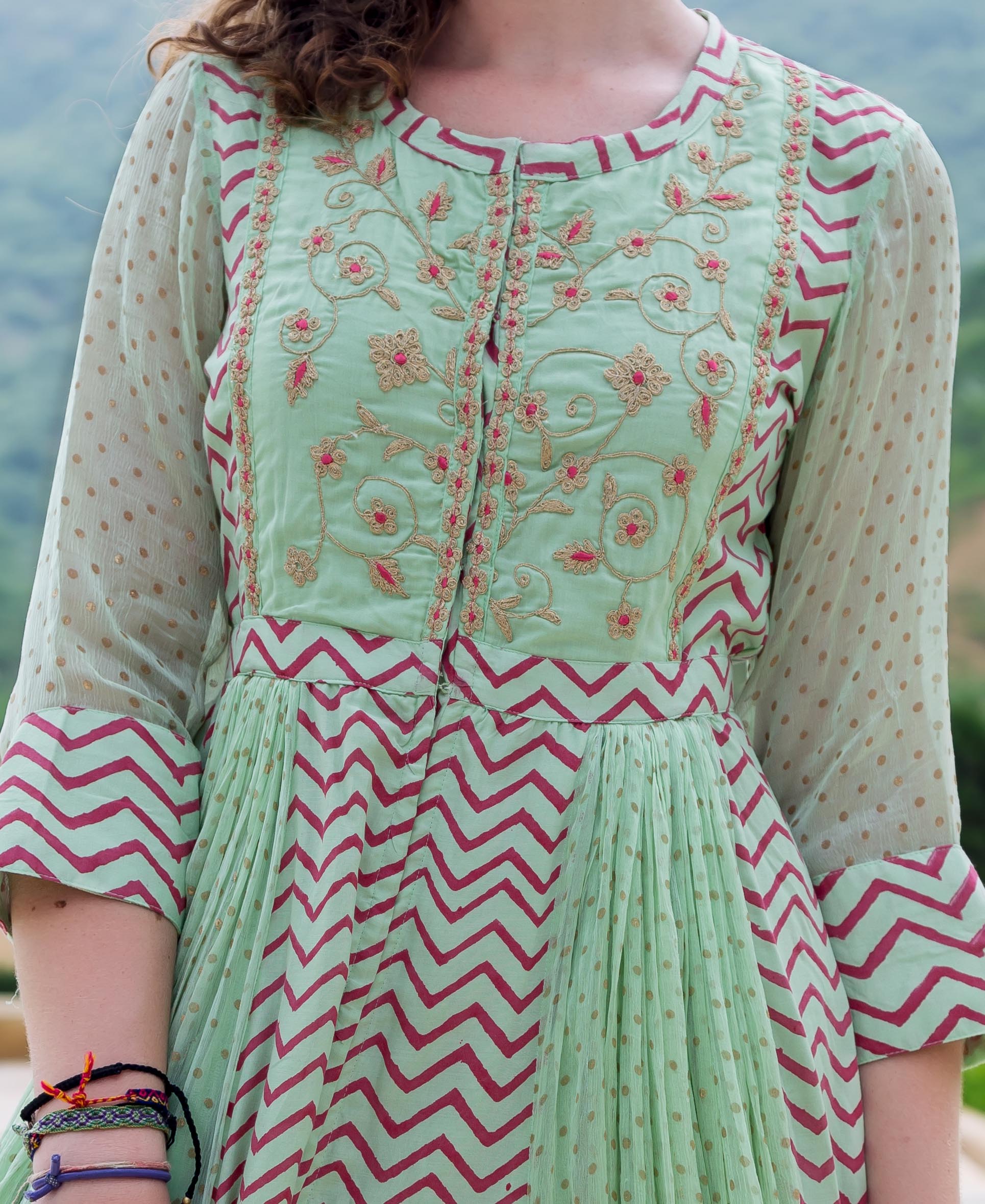 Mint green Anarkali dress with pink floral embroidery, zigzag pattern, and sheer polka dot sleeves.