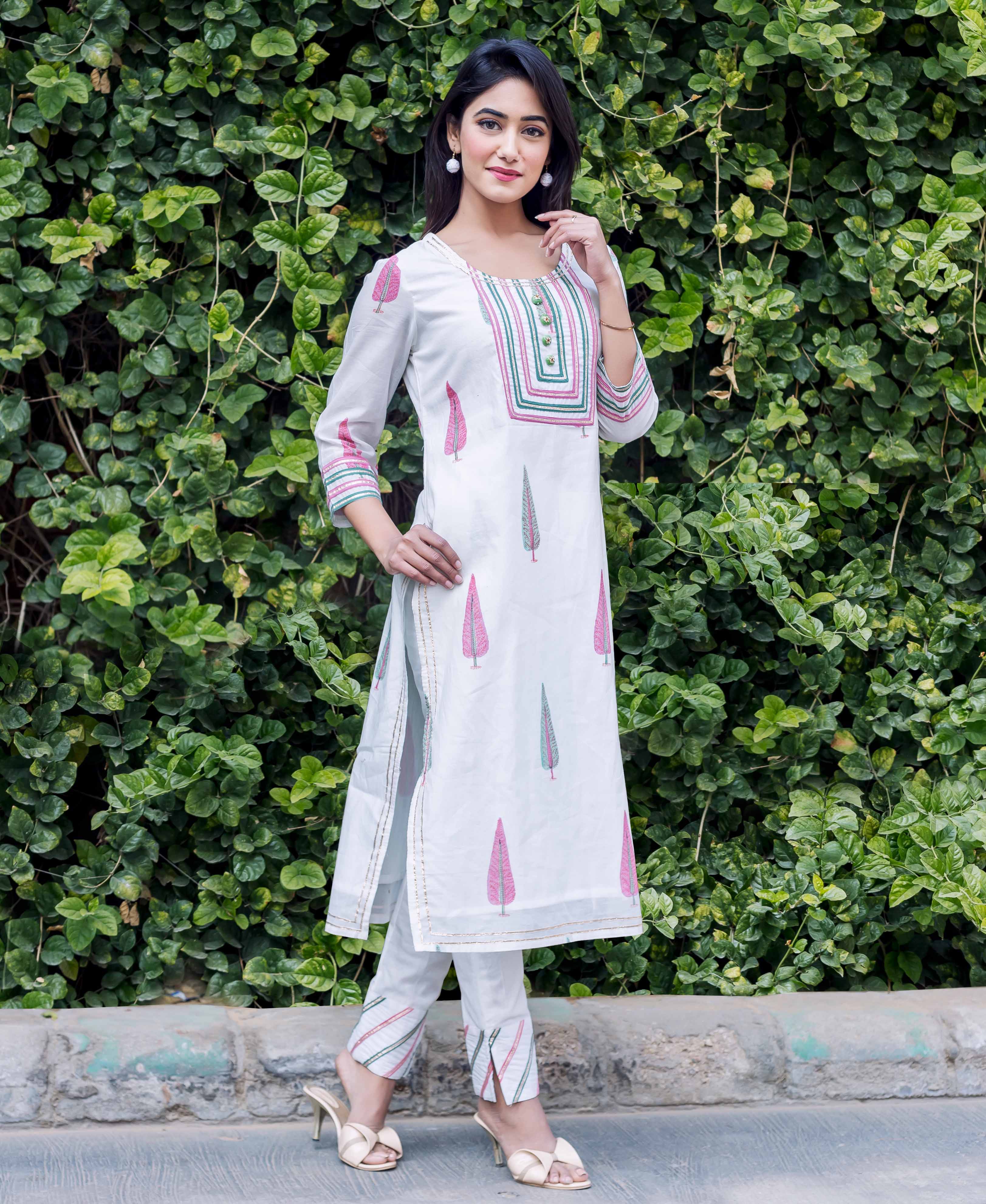 Model in white hand-block-printed kurta and pants set with pink and green patterns.