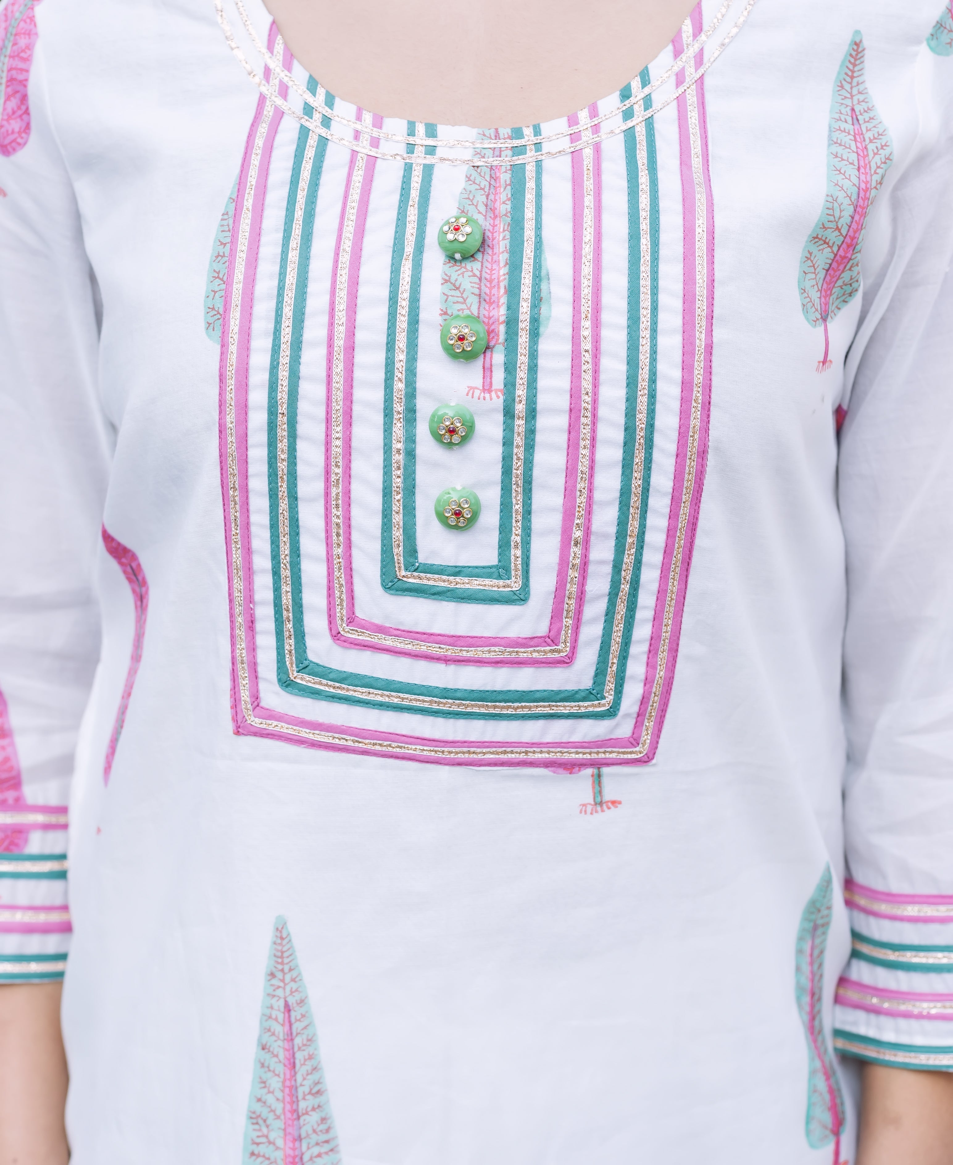 White block-printed kurta on model, with pink, teal, gold geometric neckline and green buttons.