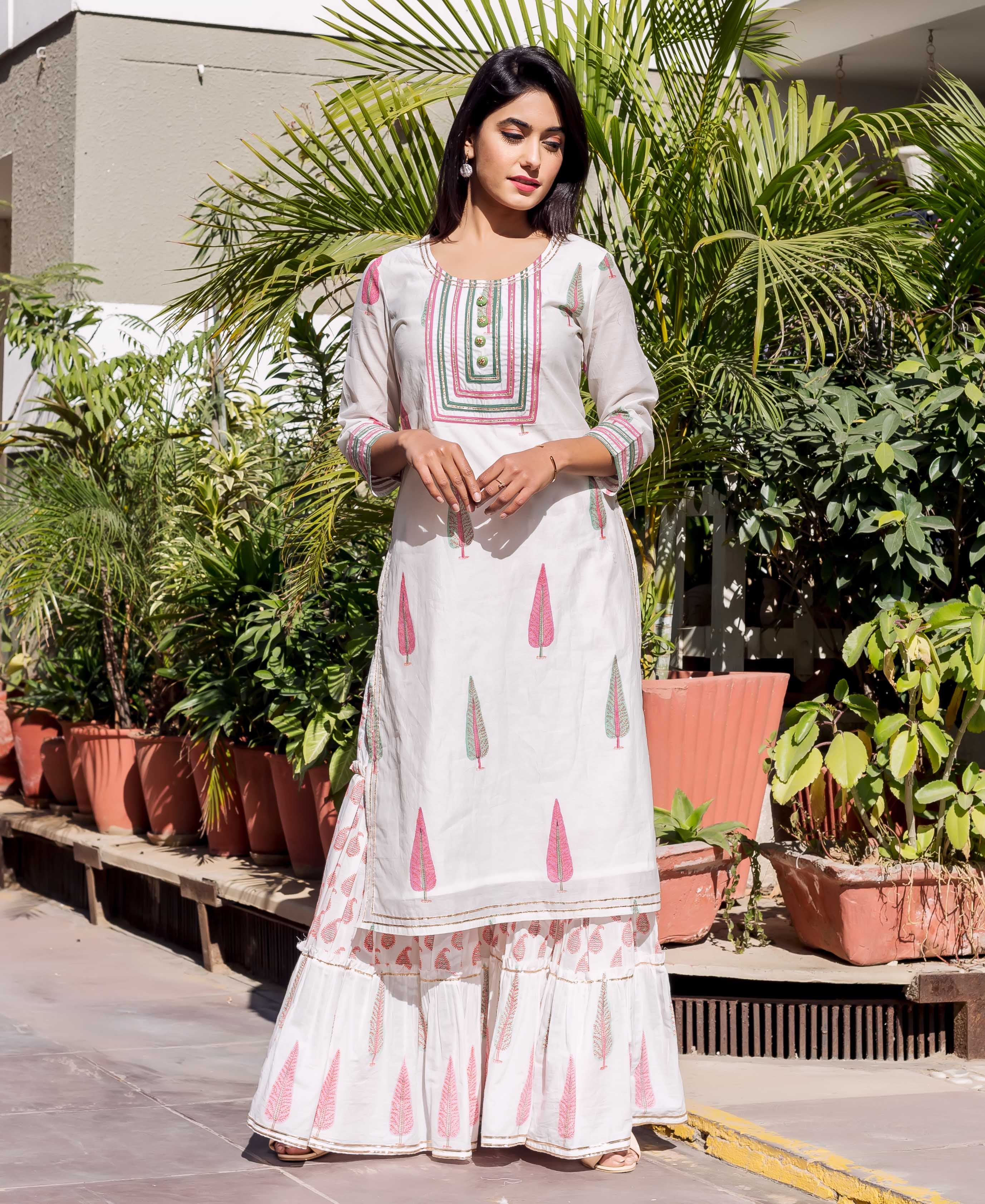 Model wears white block-printed kurta and sharara set with pink and green leaves.