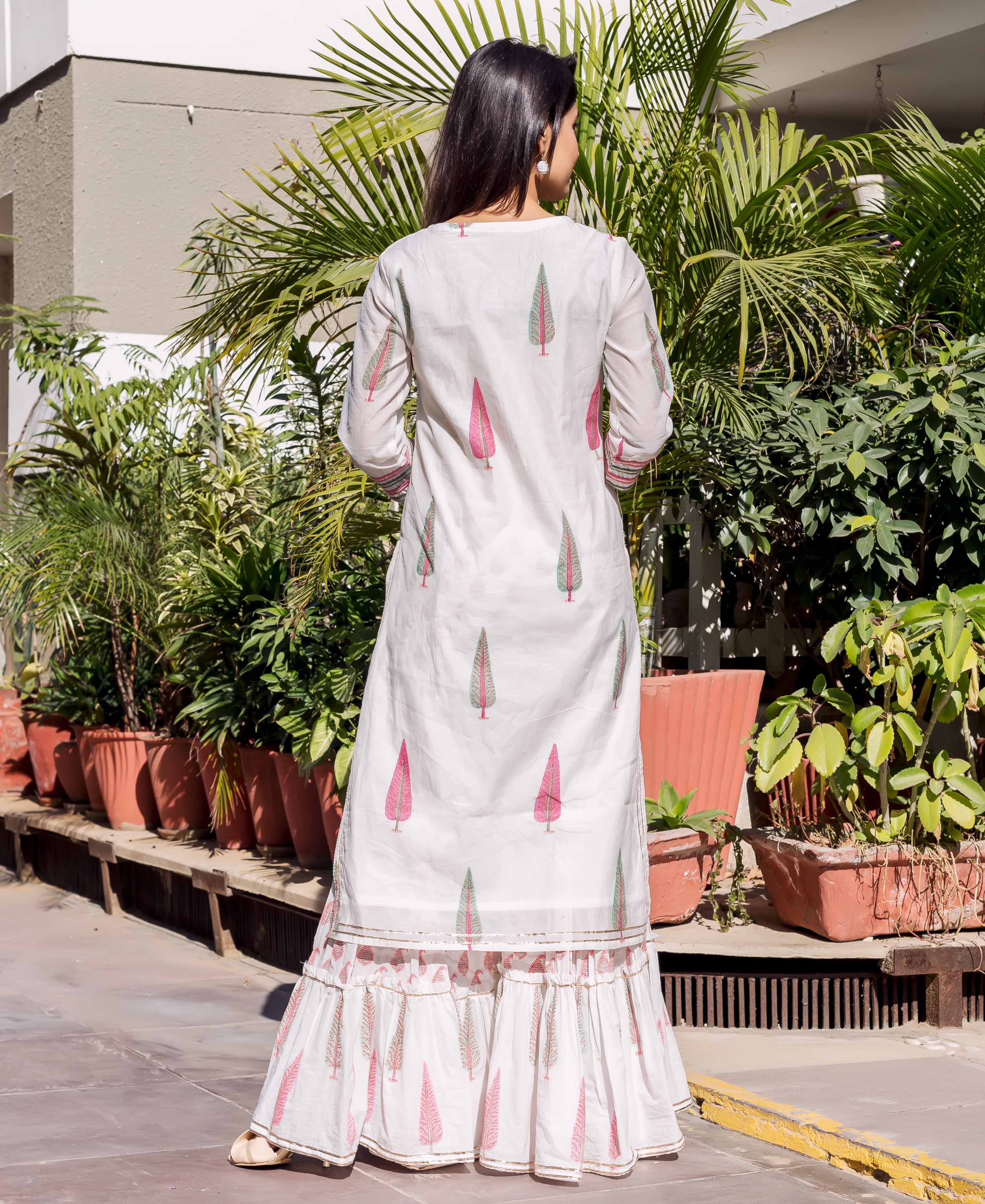 Back view of model in white kurta and tiered sharara with pink and green tree prints.