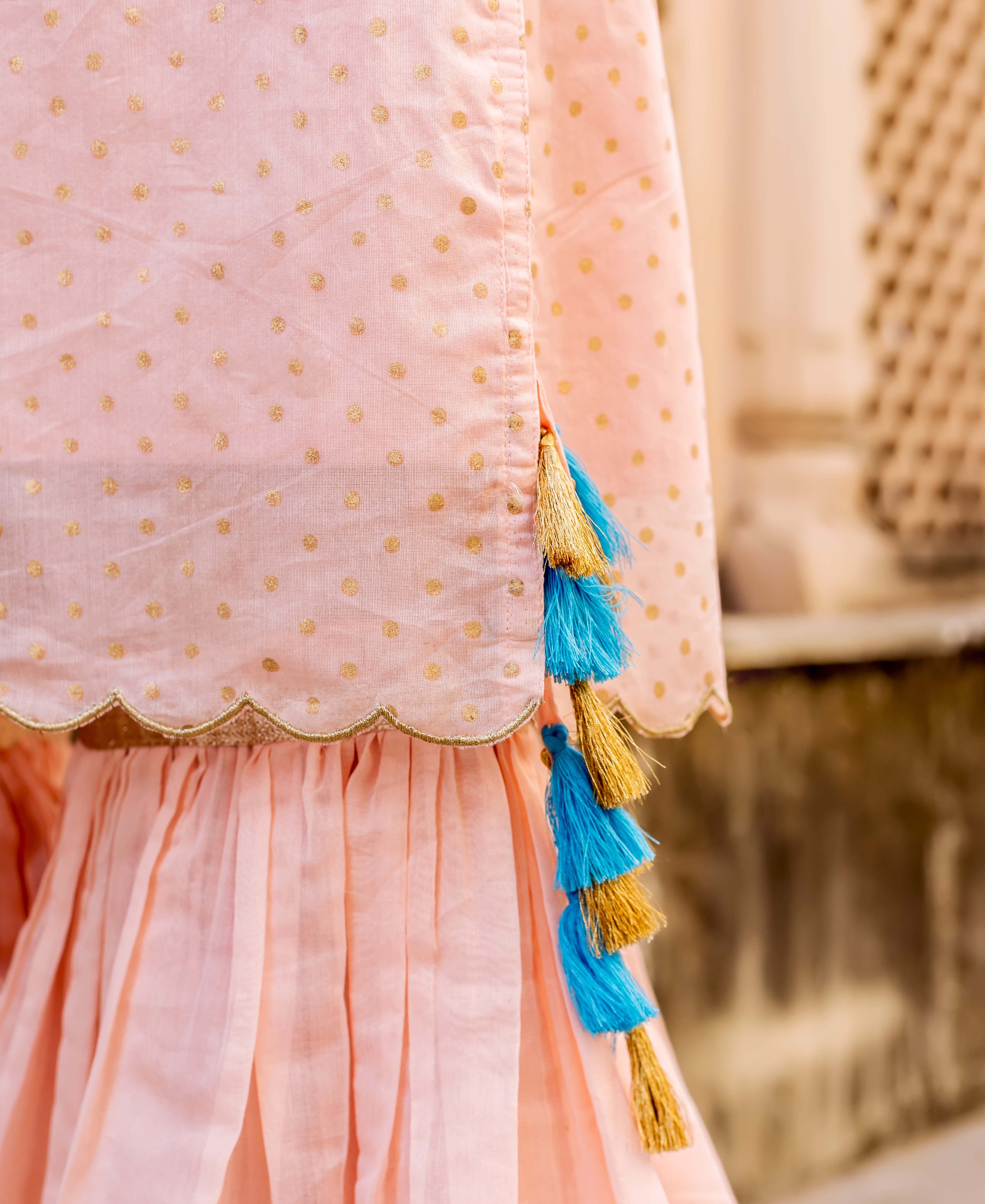 Close-up of peach polka dot kurta with scalloped gold trim and blue-gold tassels.