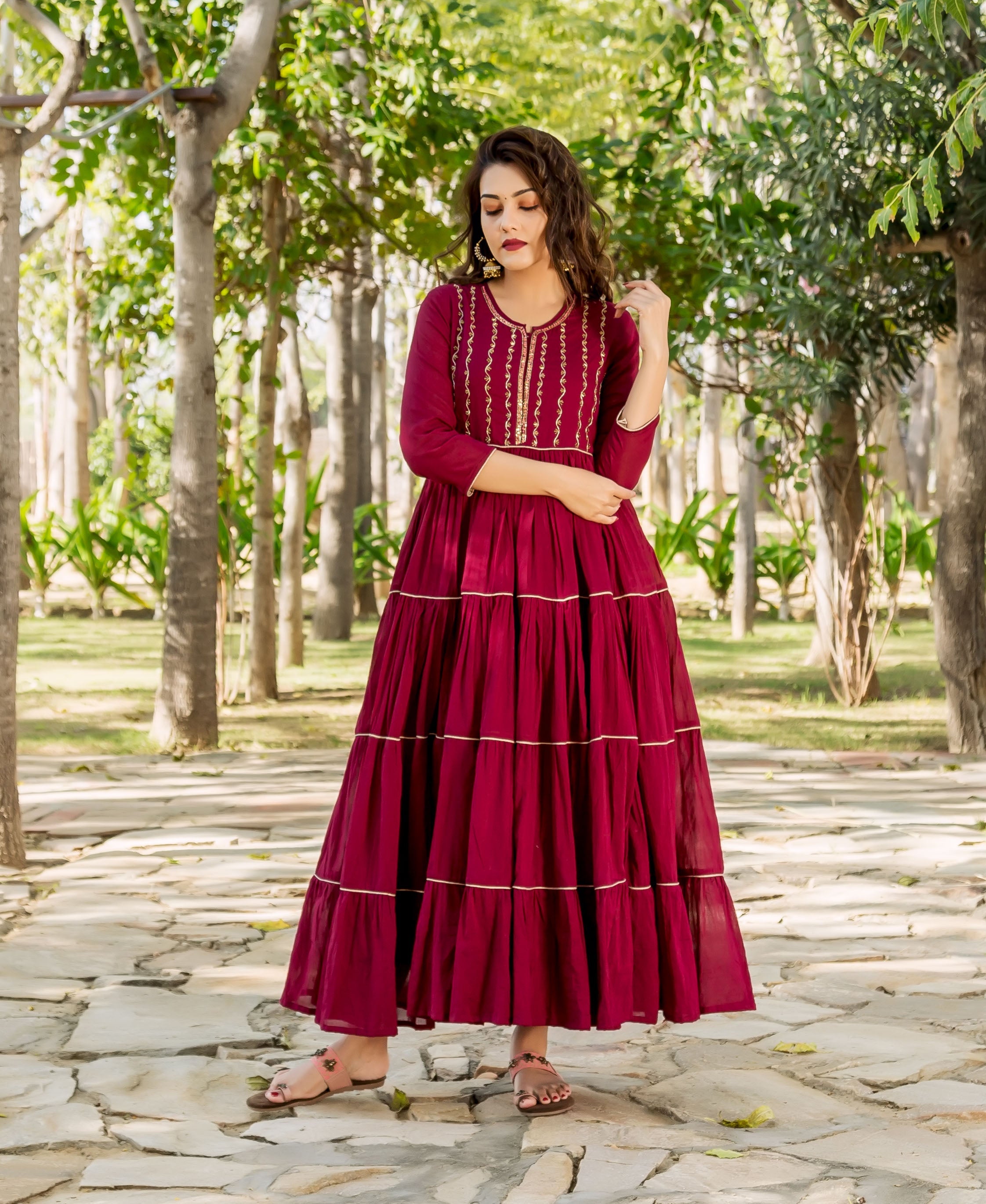 Model in a full-length maroon tiered dress with gold hand embroidery.