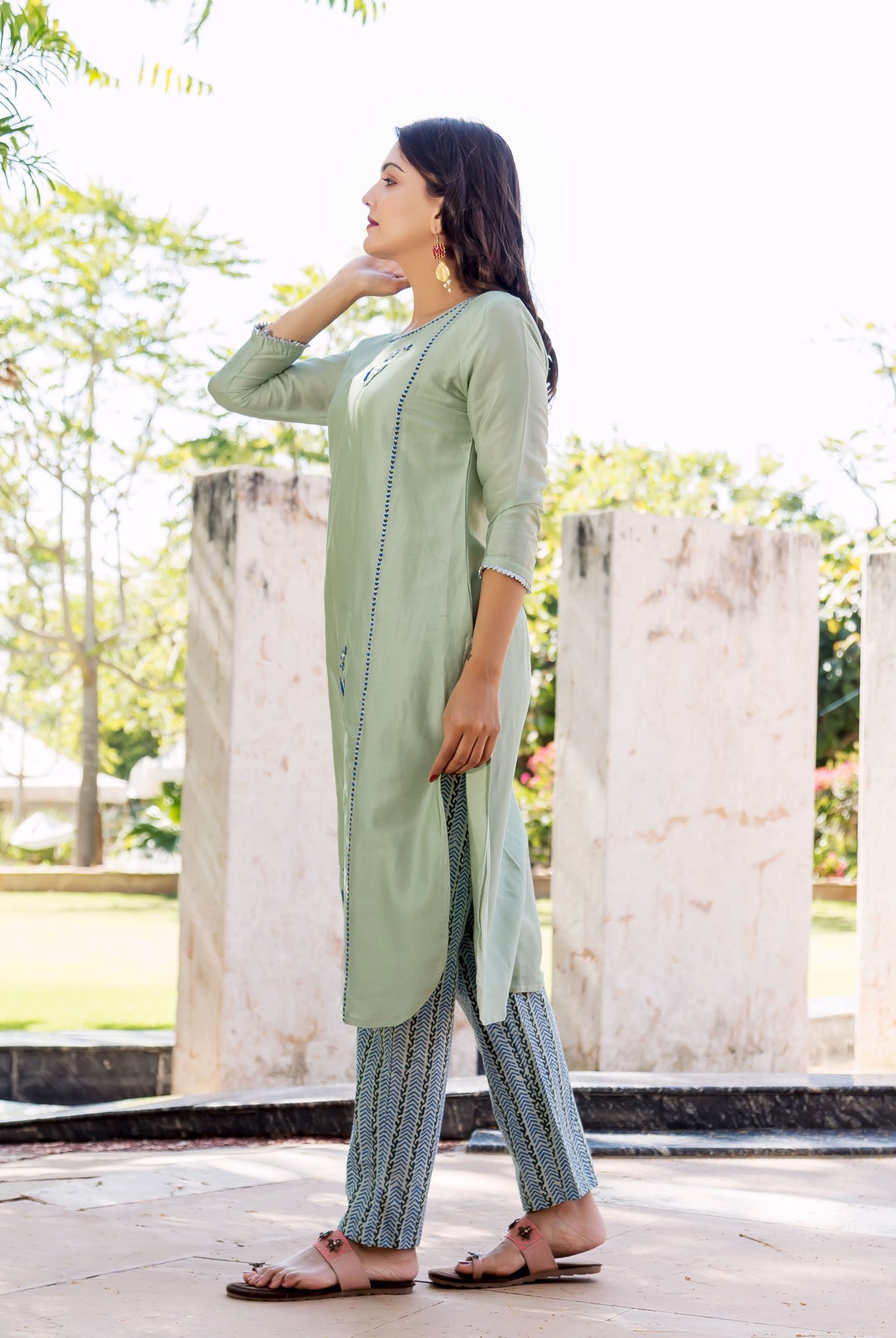 Side profile of model wearing pistachio green hand-embroidered kurta and blue patterned pants.