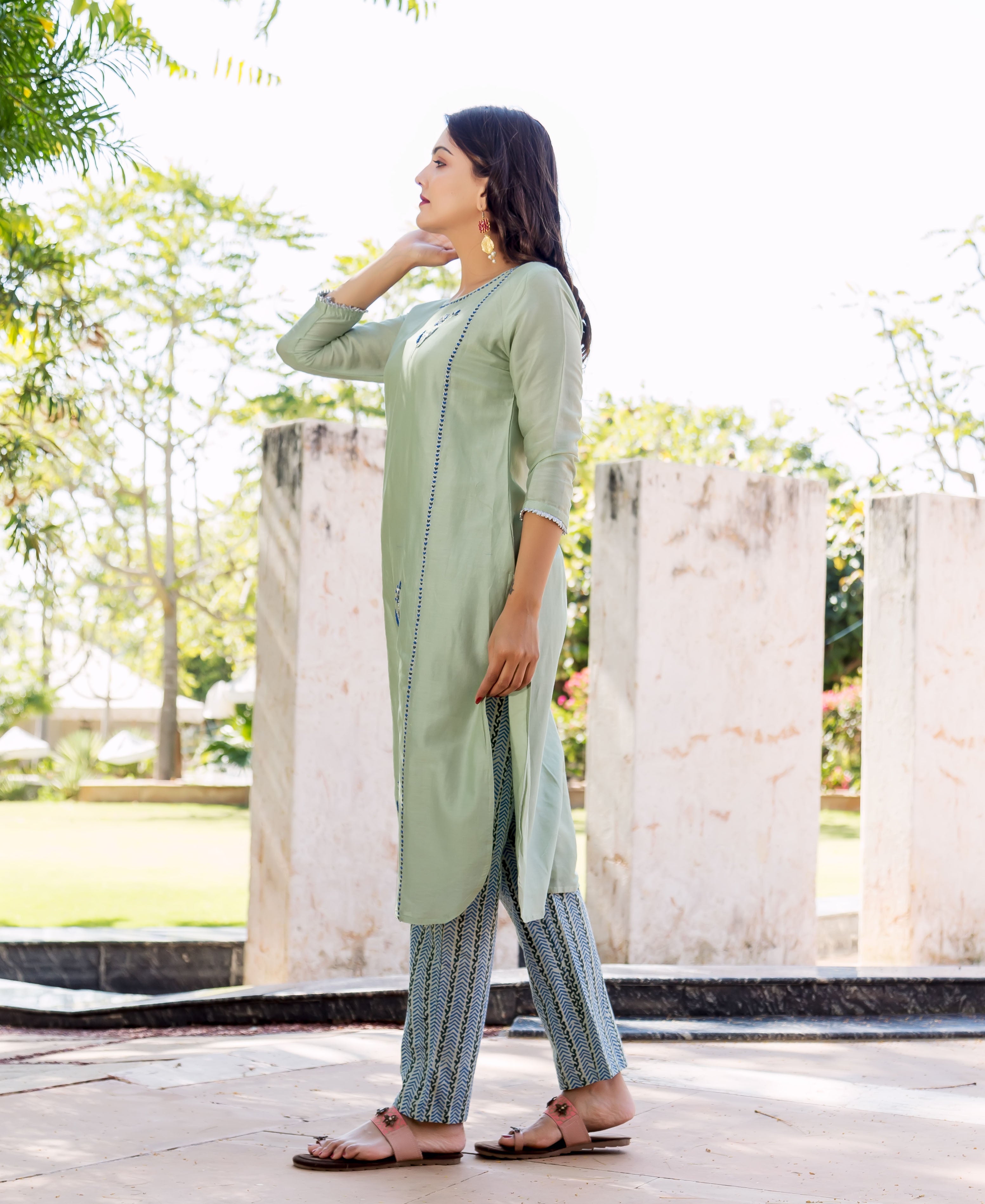 Side profile of model wearing pistachio green hand-embroidered kurta and blue patterned pants.