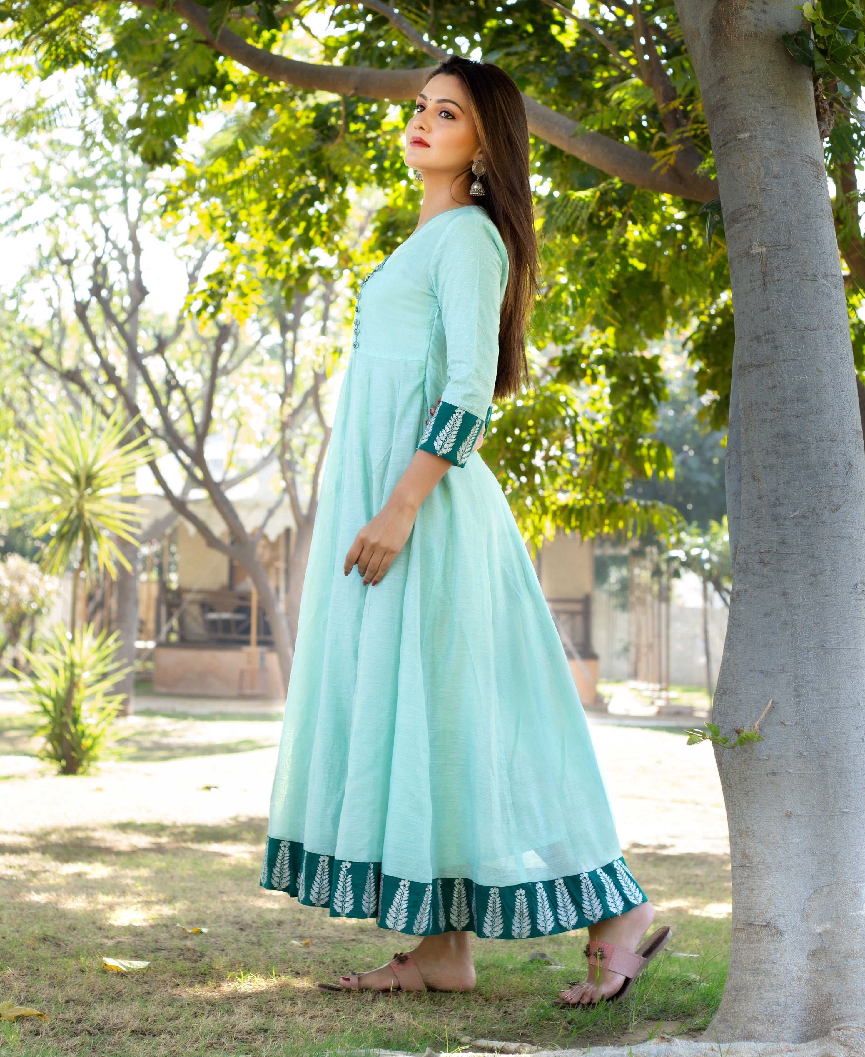 Model poses in a mint green ethnic dress with dark green leaf motif border.