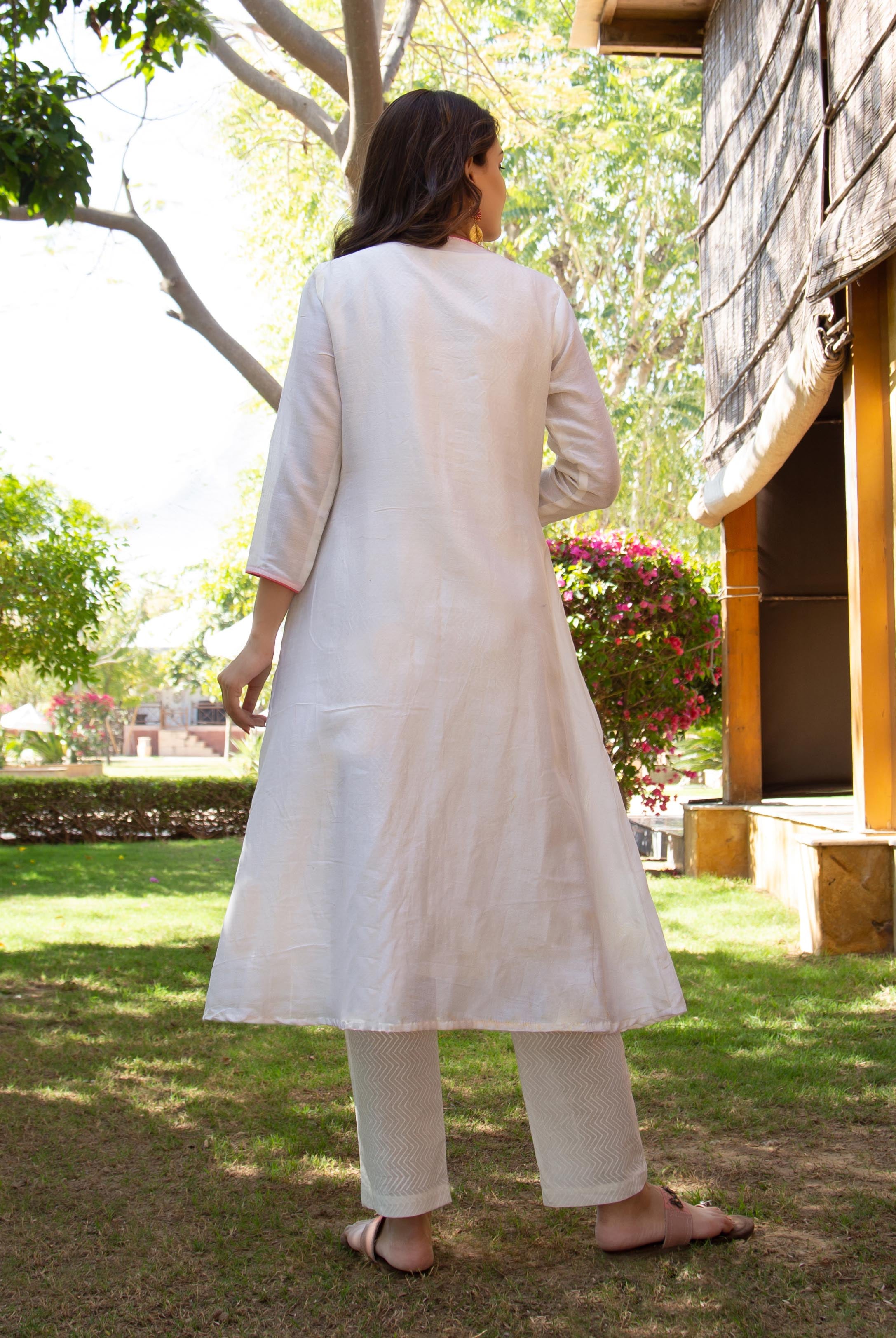 Back view of woman in white kurta and white zigzag patterned pants in a garden.