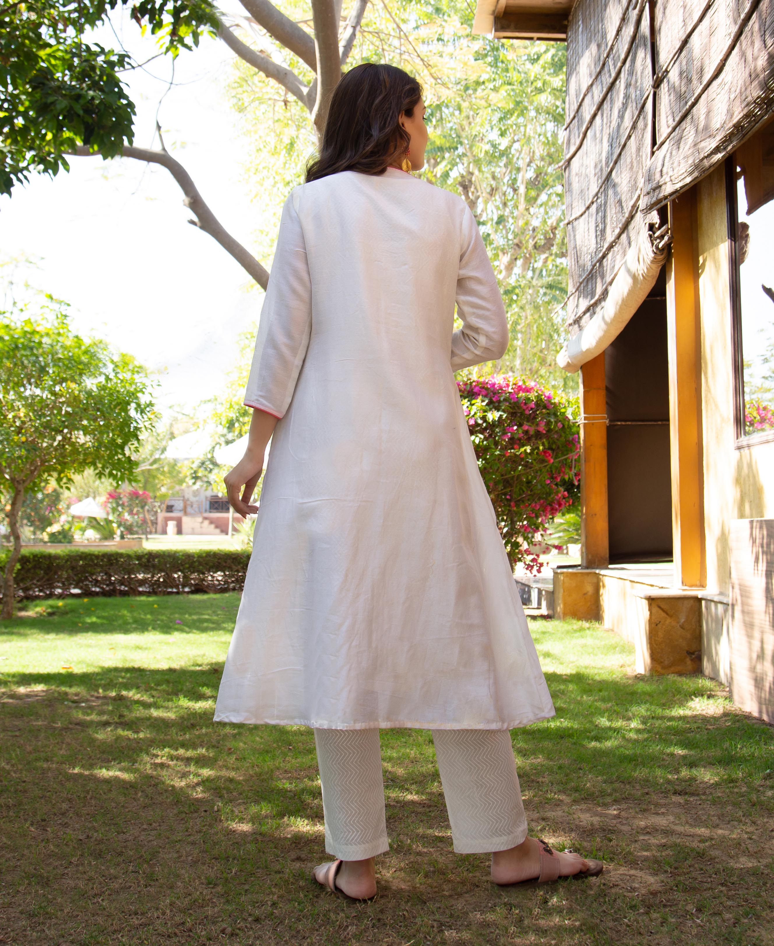 Back view of woman in white kurta and white zigzag patterned pants in a garden.