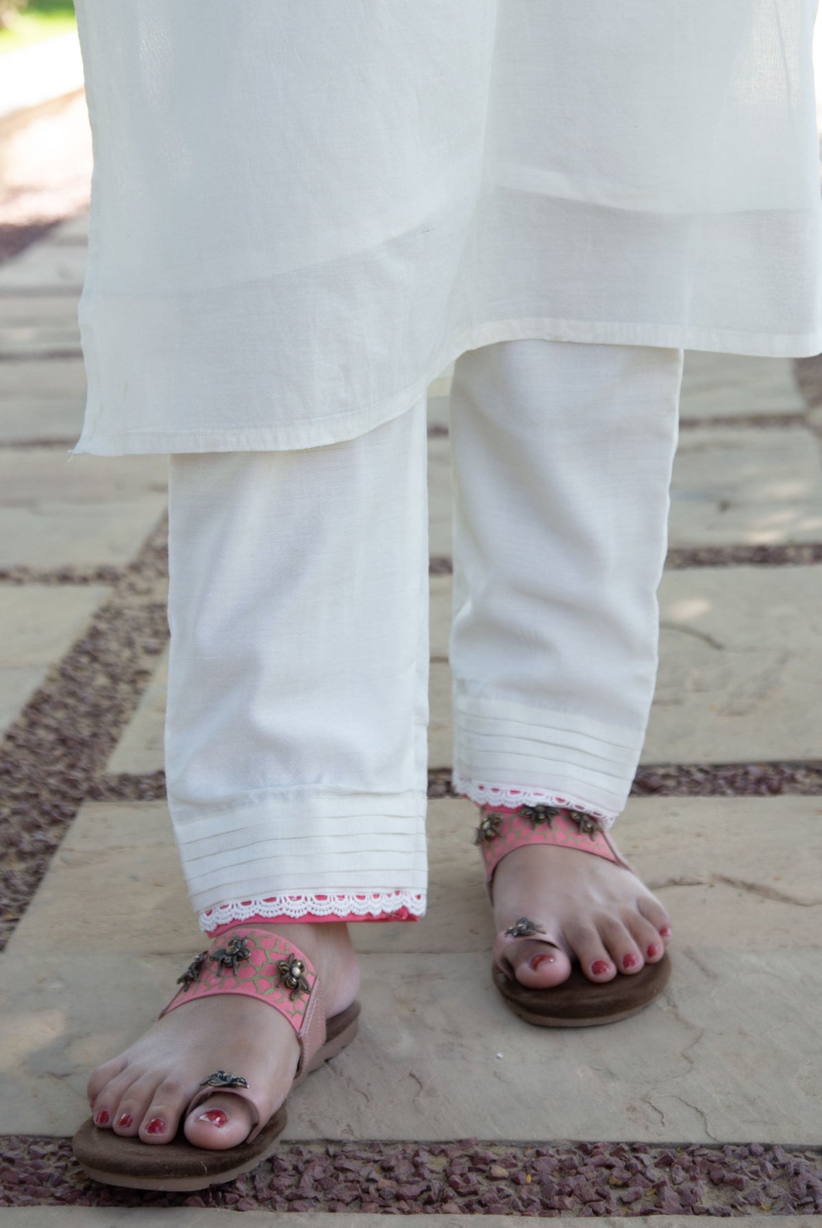 Close-up of model's feet in pink ethnic printed sandals, white pants with lace.