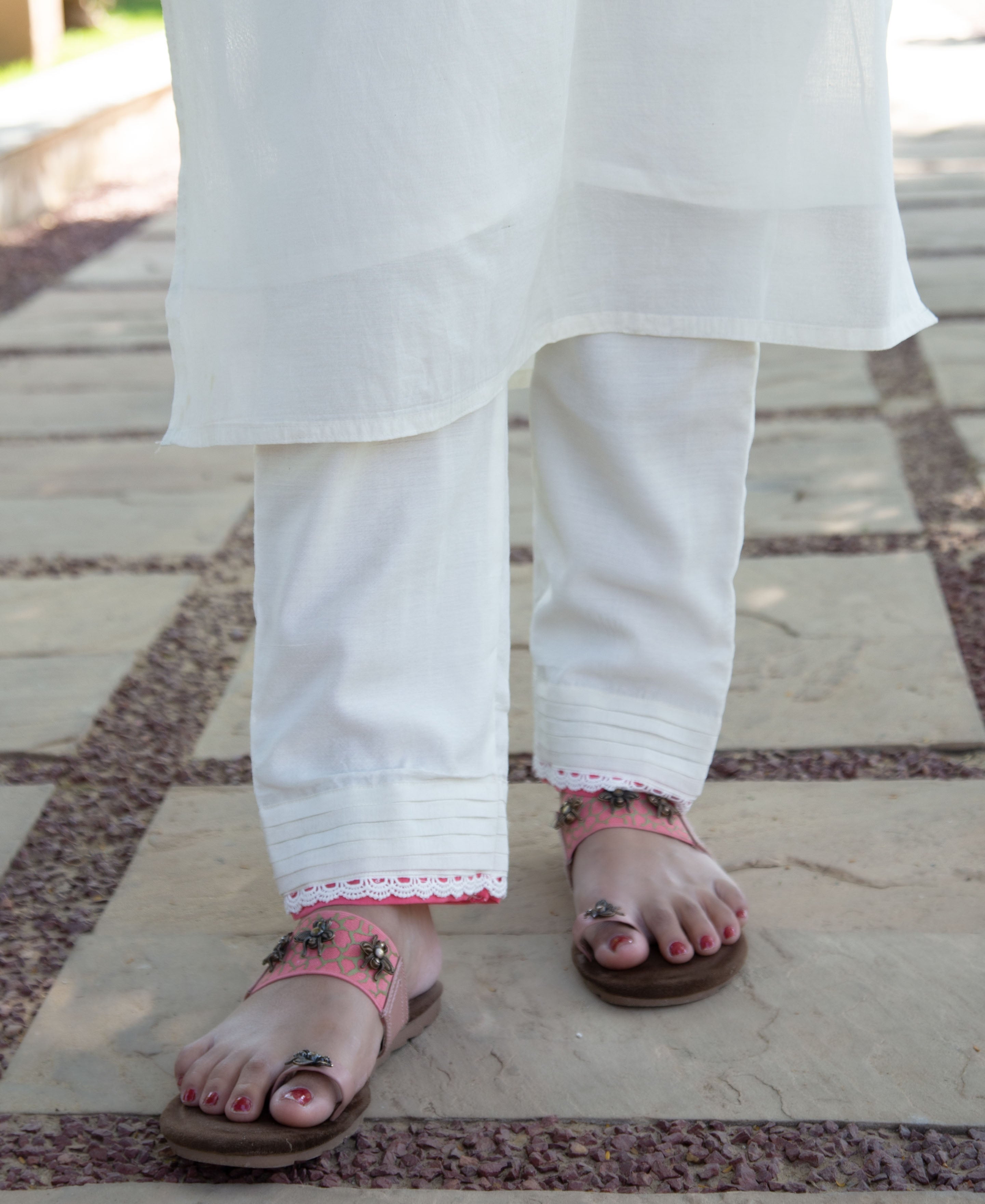 Close-up of model's feet in pink ethnic printed sandals, white pants with lace.