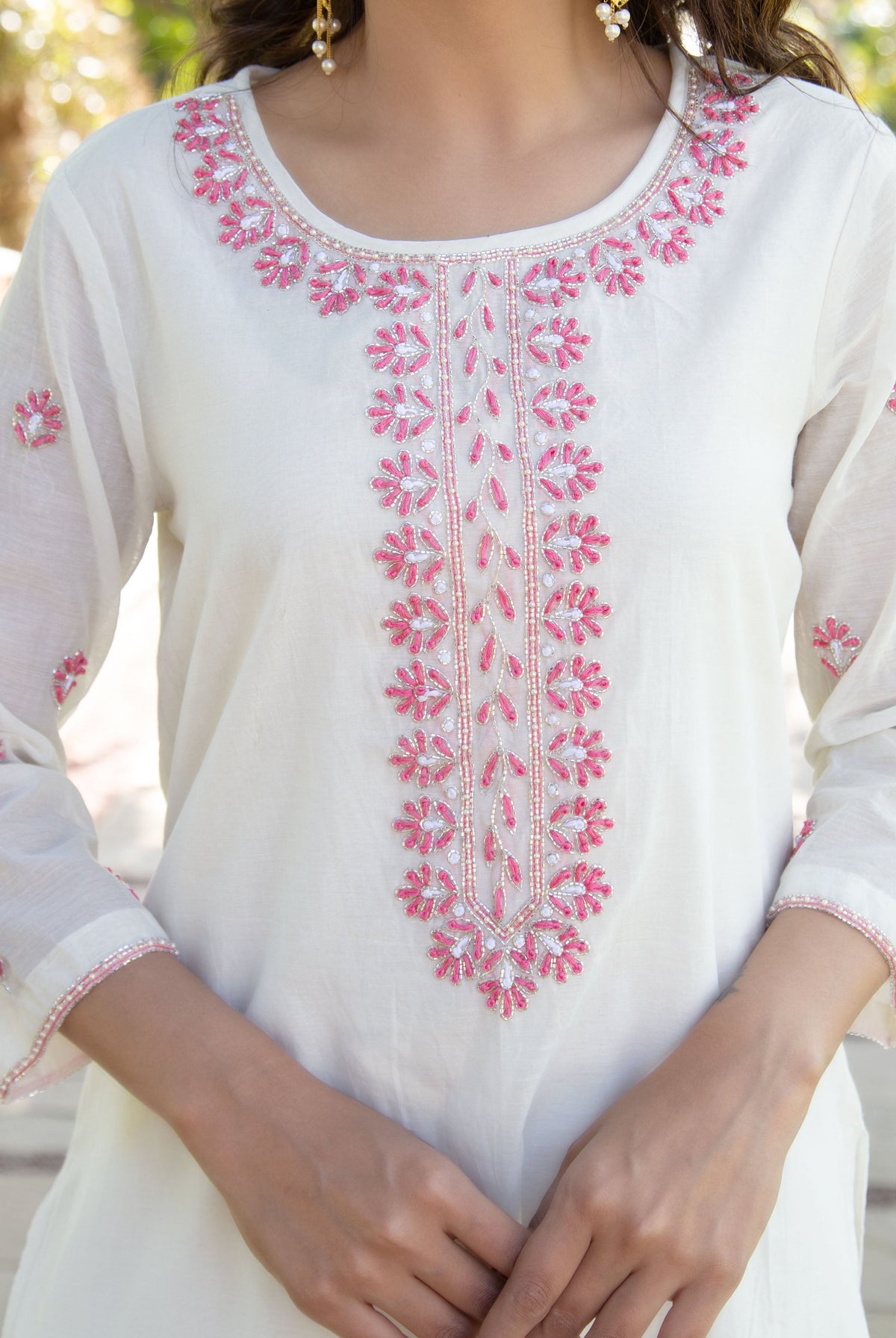 Model wearing an off-white kurta with intricate pink floral embroidery and silver beadwork.