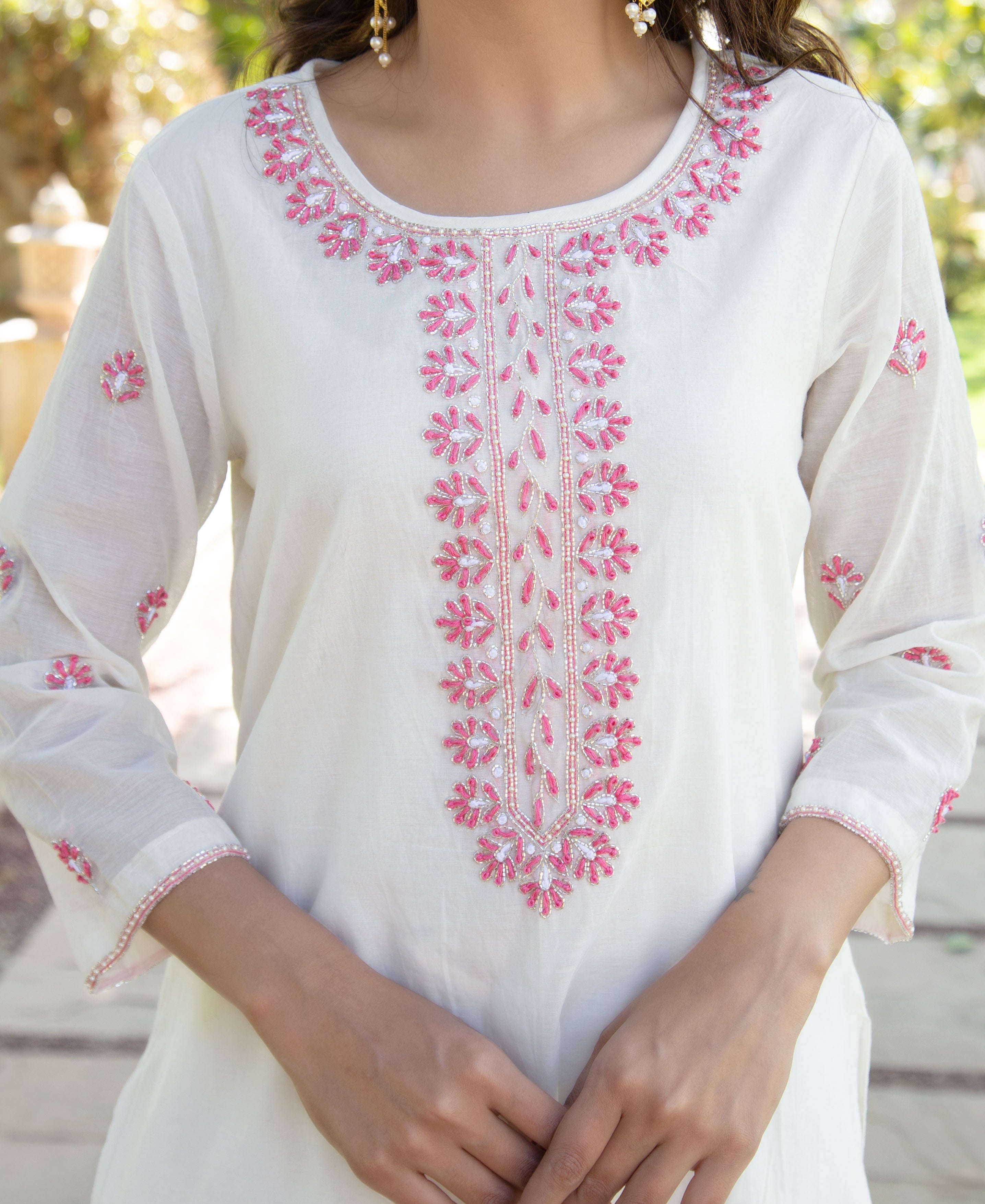 Model wearing an off-white kurta with intricate pink floral embroidery and silver beadwork.