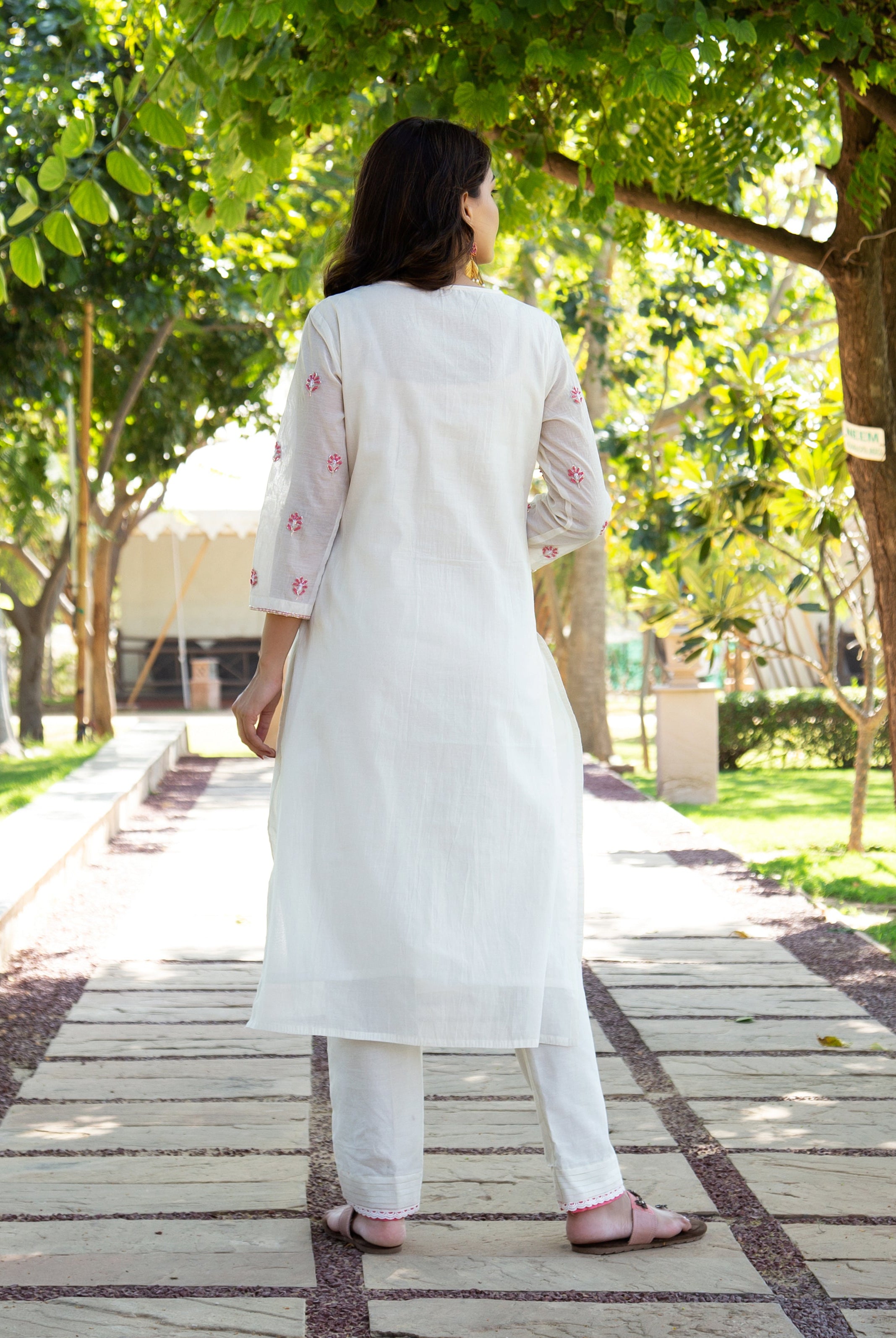 Rear view of woman in white hand-block printed kurta set with pink floral details.