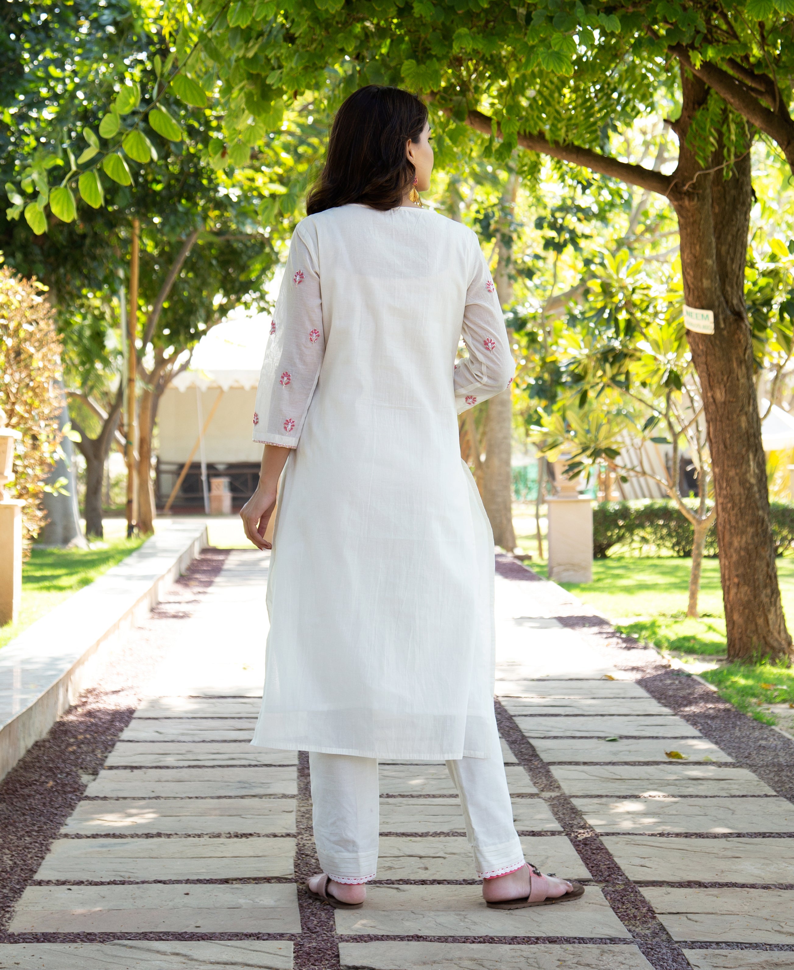 Rear view of woman in white hand-block printed kurta set with pink floral details.