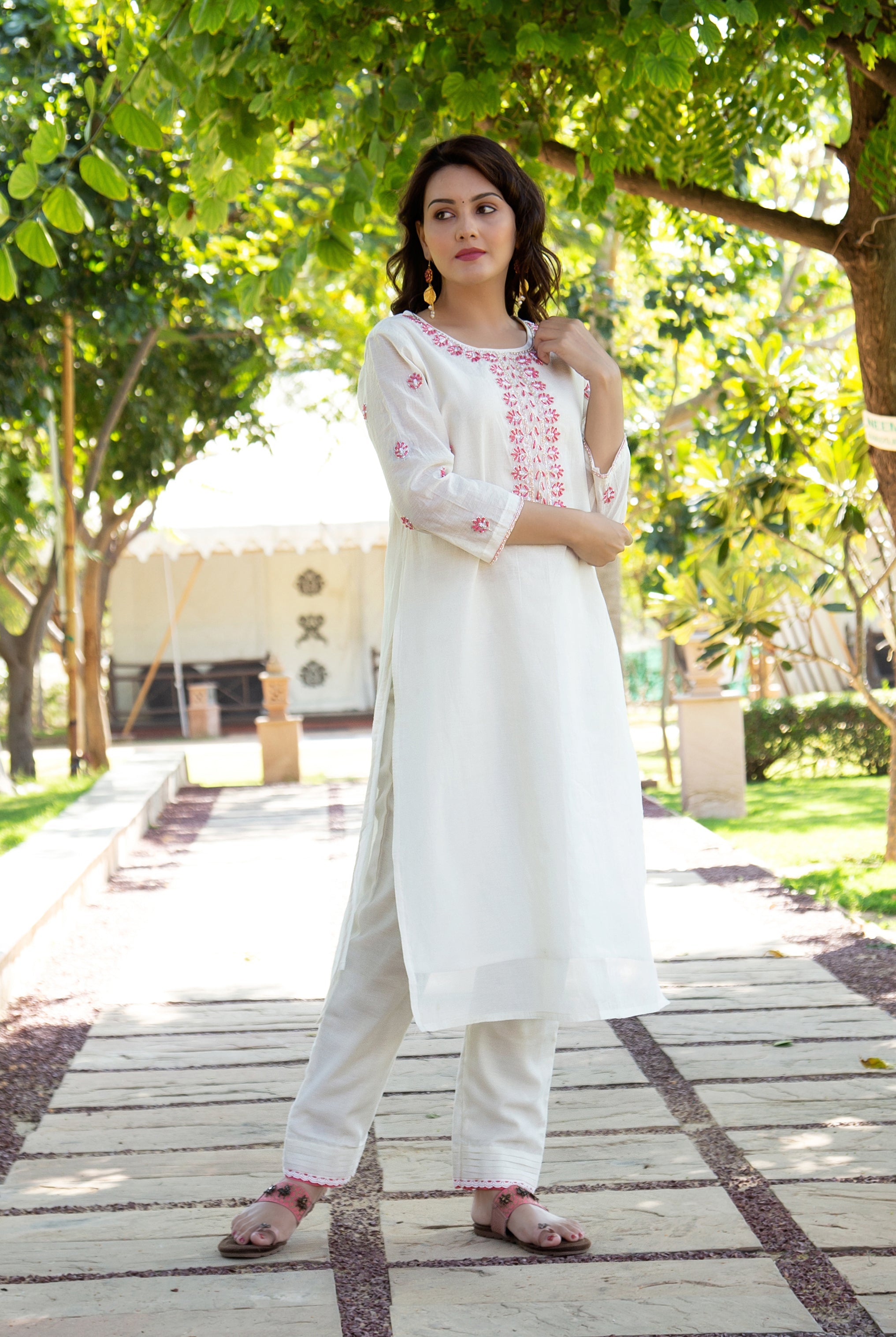 Model in white embroidered kurta and trousers, featuring pink floral patterns outdoors.