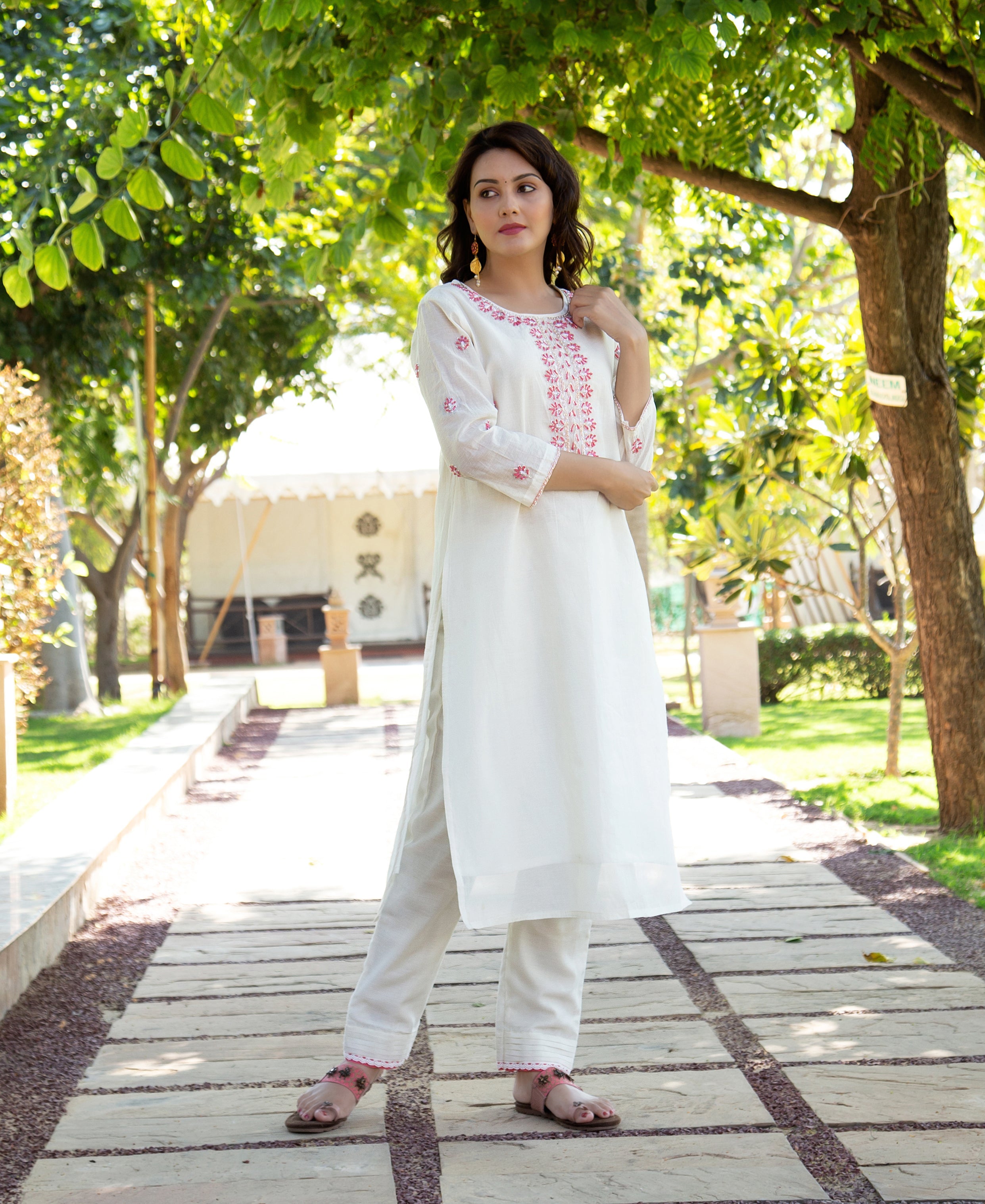 Model in white embroidered kurta and trousers, featuring pink floral patterns outdoors.