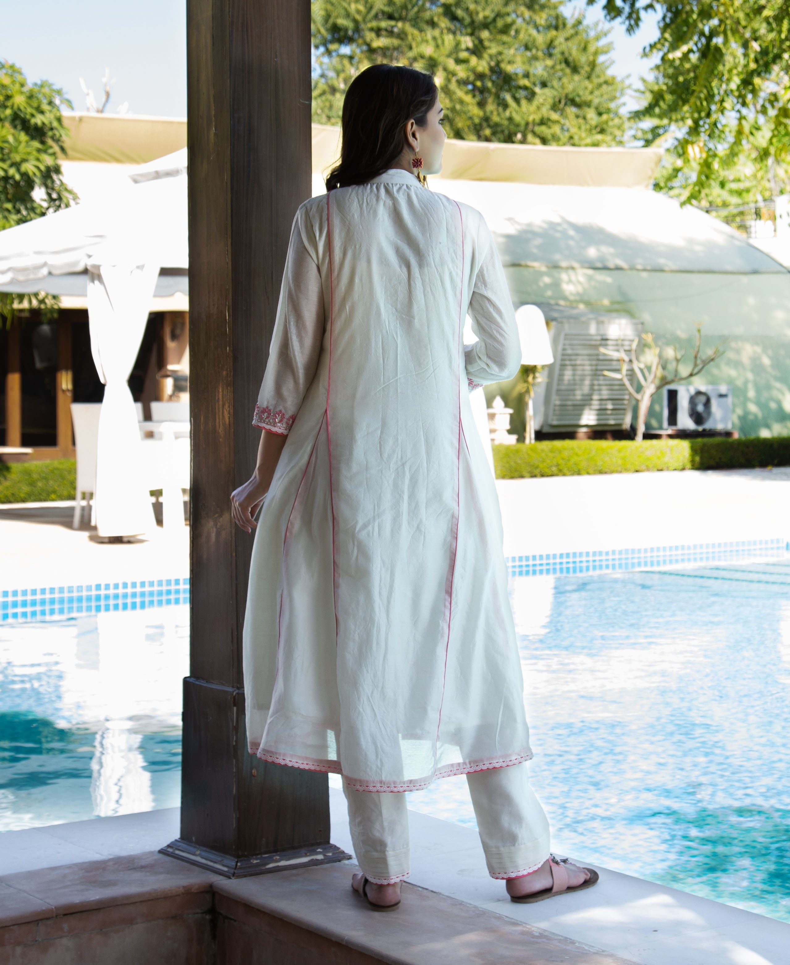 Back view of a model in white A-line kurta with pink embroidered details and trim.