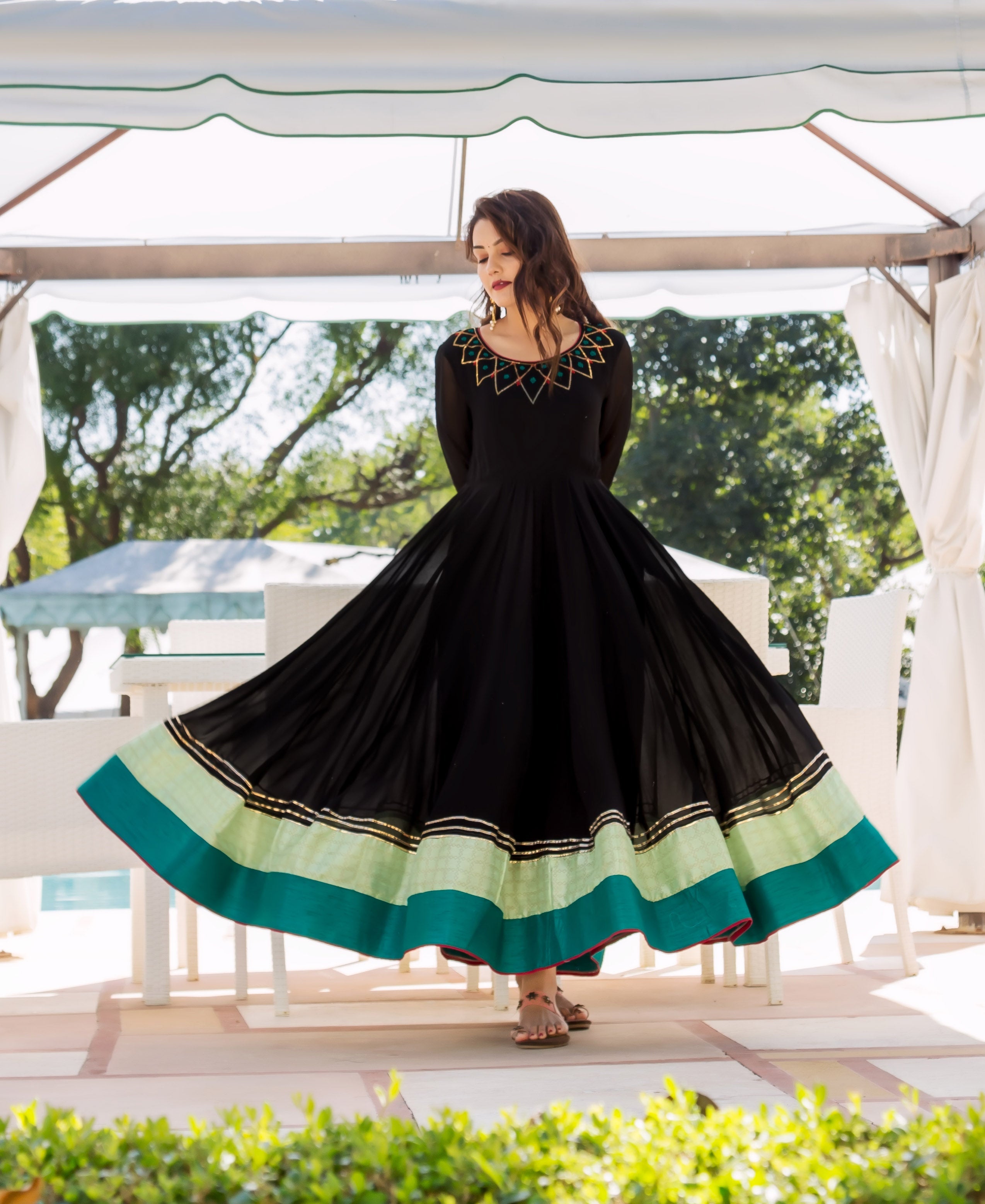 Full view of a model in a black Anarkali dress with ethnic embroidery and lime-teal hem.