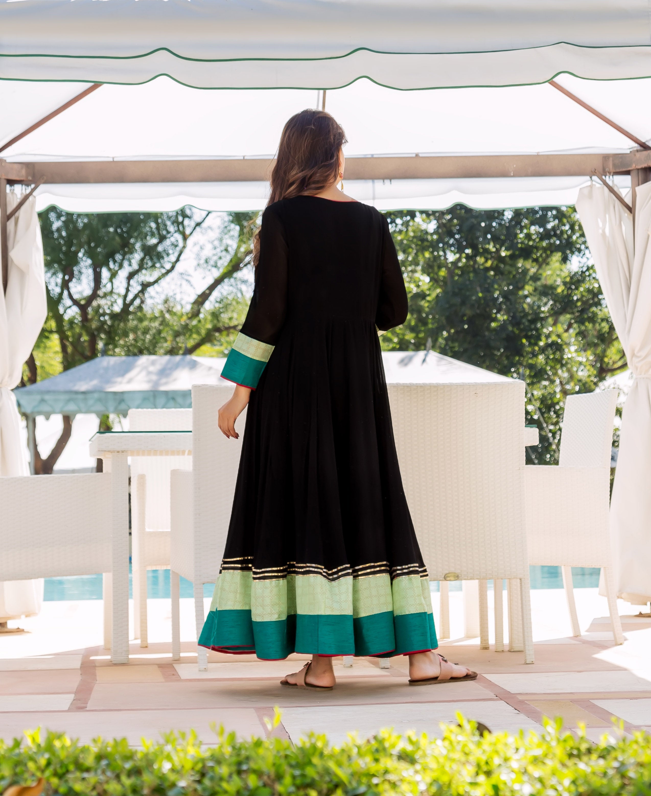 Model from back in black Anarkali dress with lime, teal borders, and gold accents.