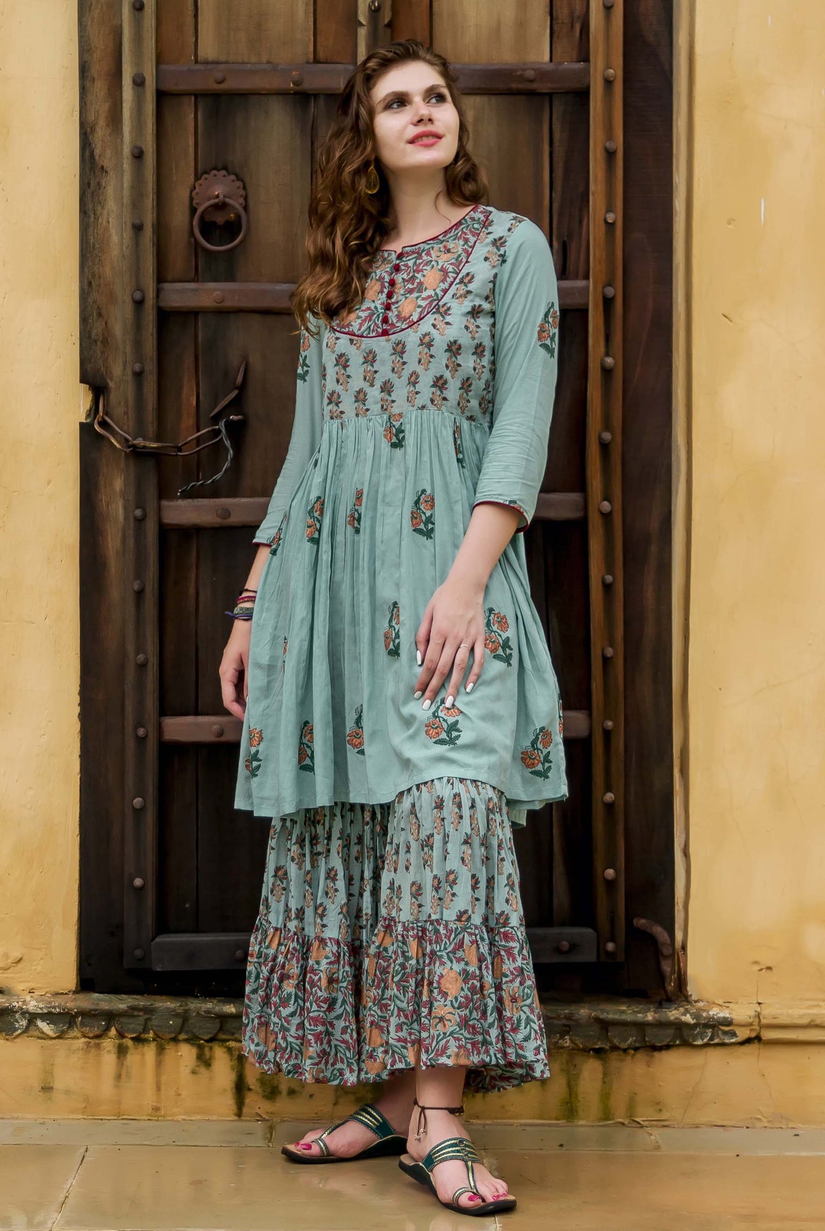 Model stands in dusty teal hand-block printed kurta and sharara set with floral patterns.