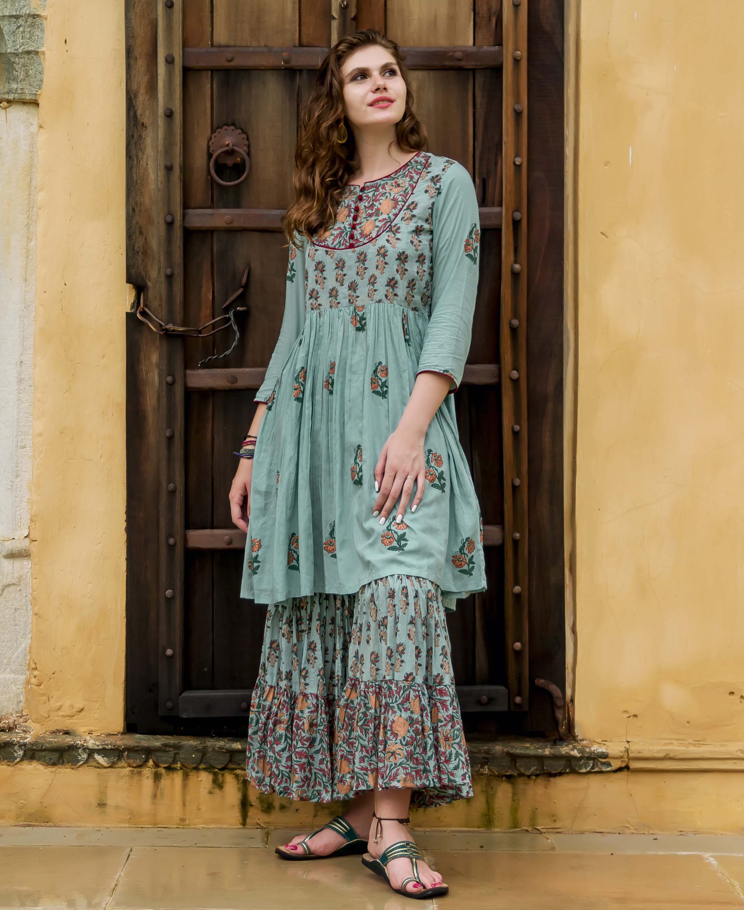 Model stands in dusty teal hand-block printed kurta and sharara set with floral patterns.