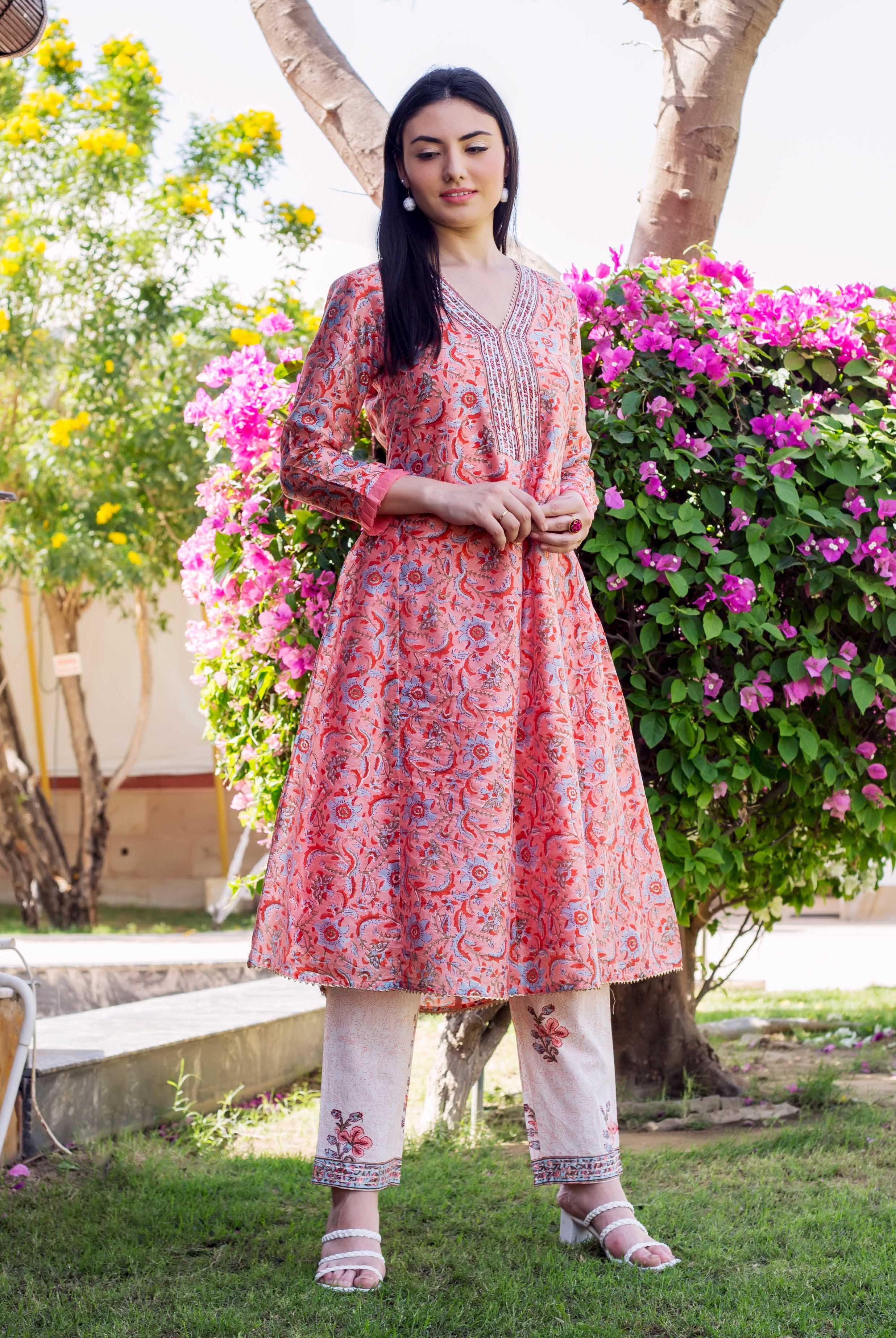 Woman wearing a peach floral block-printed A-line kurta set and cream pants with white heels.