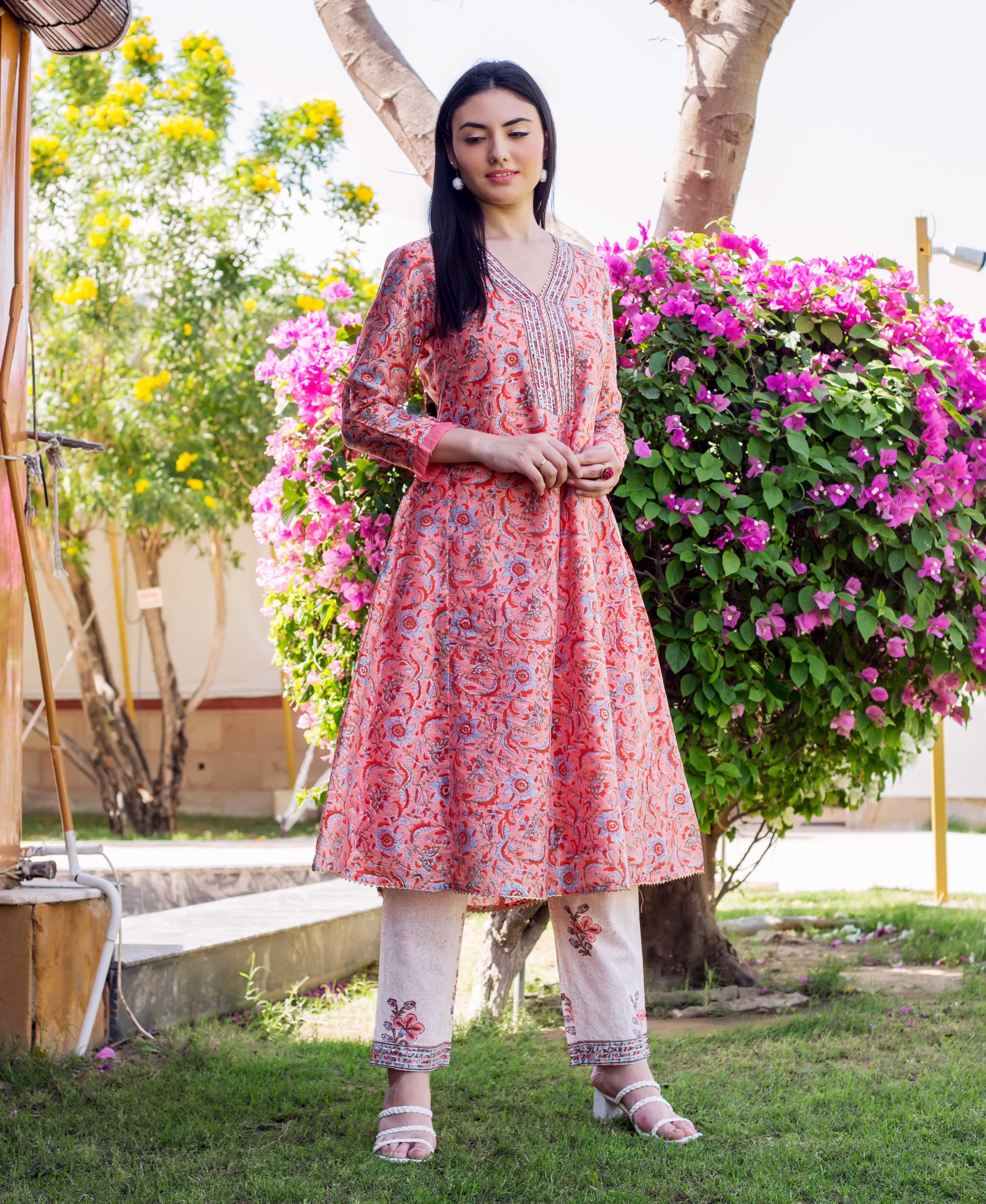 Woman wearing a peach floral block-printed A-line kurta set and cream pants with white heels.