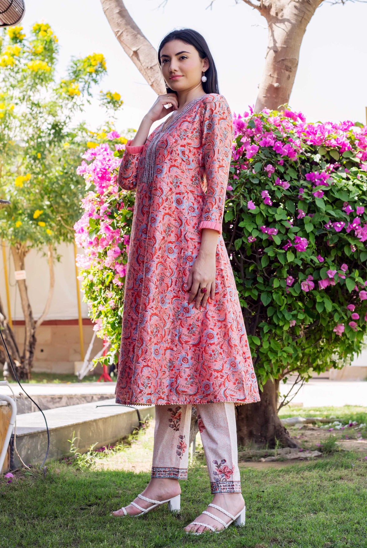 Standing woman in coral block-printed A-line kurta with blue pattern and white printed pants.