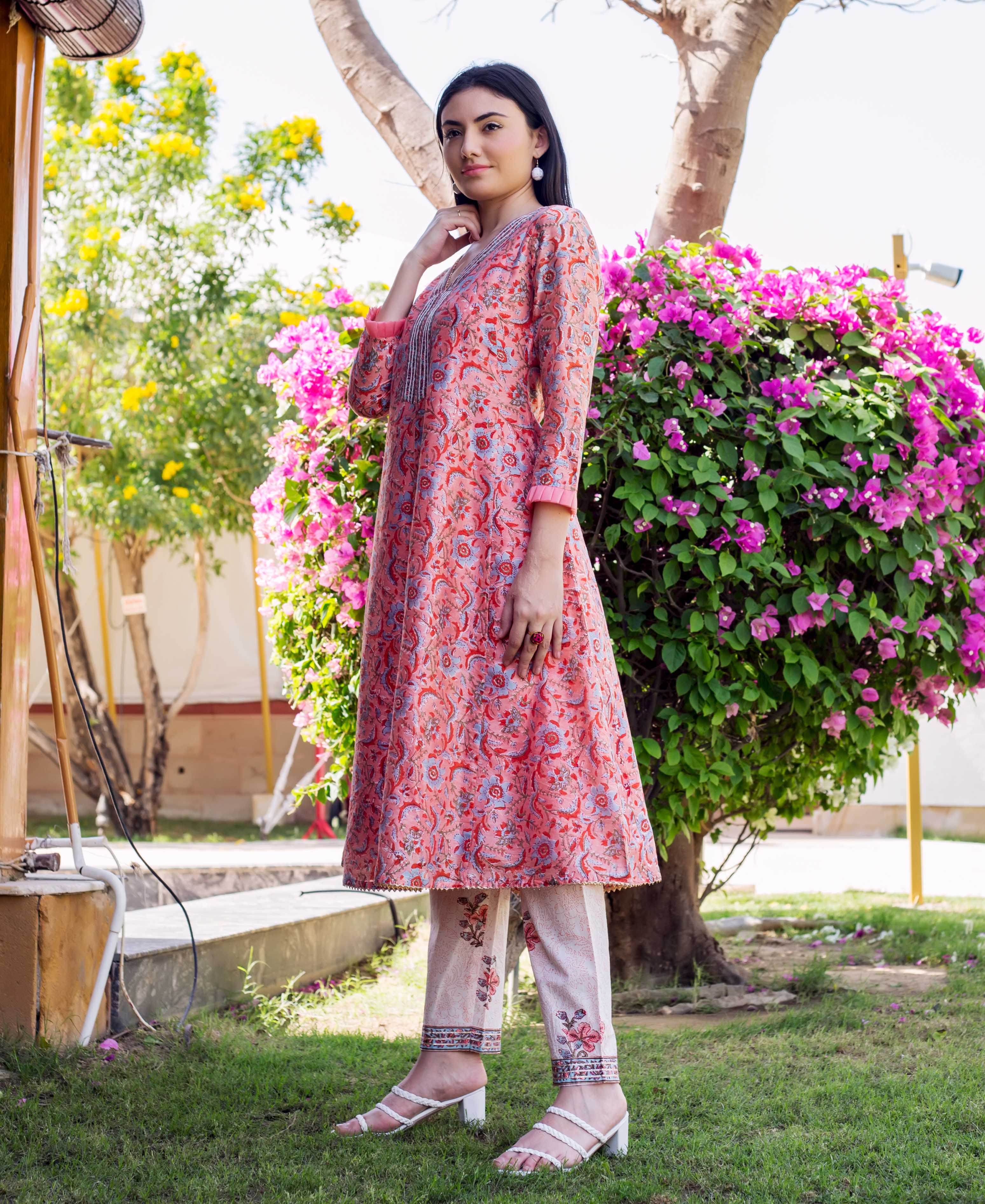 Standing woman in coral block-printed A-line kurta with blue pattern and white printed pants.