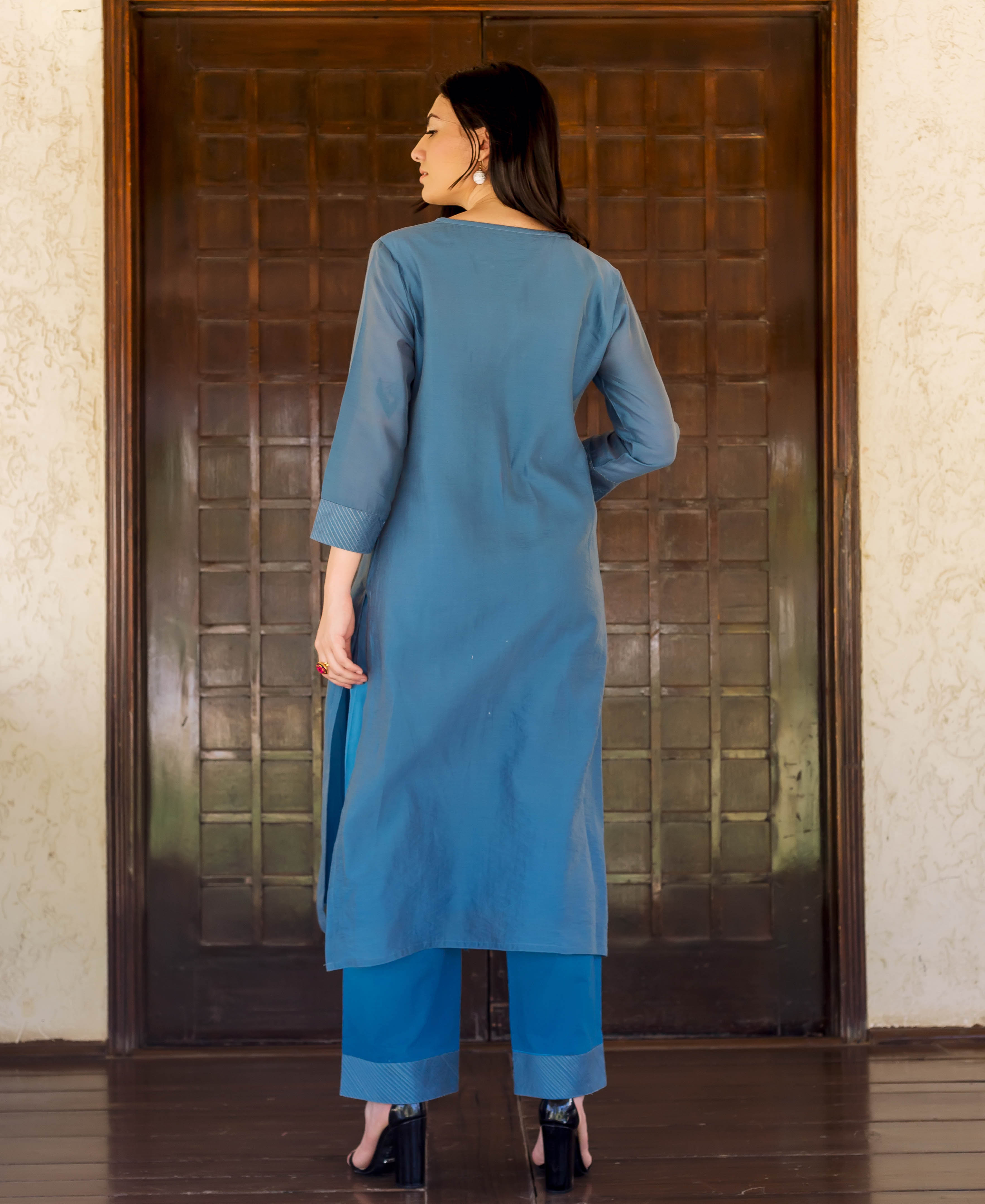 Model in Prussian blue kurta and pants, seen from the back with striped hems.