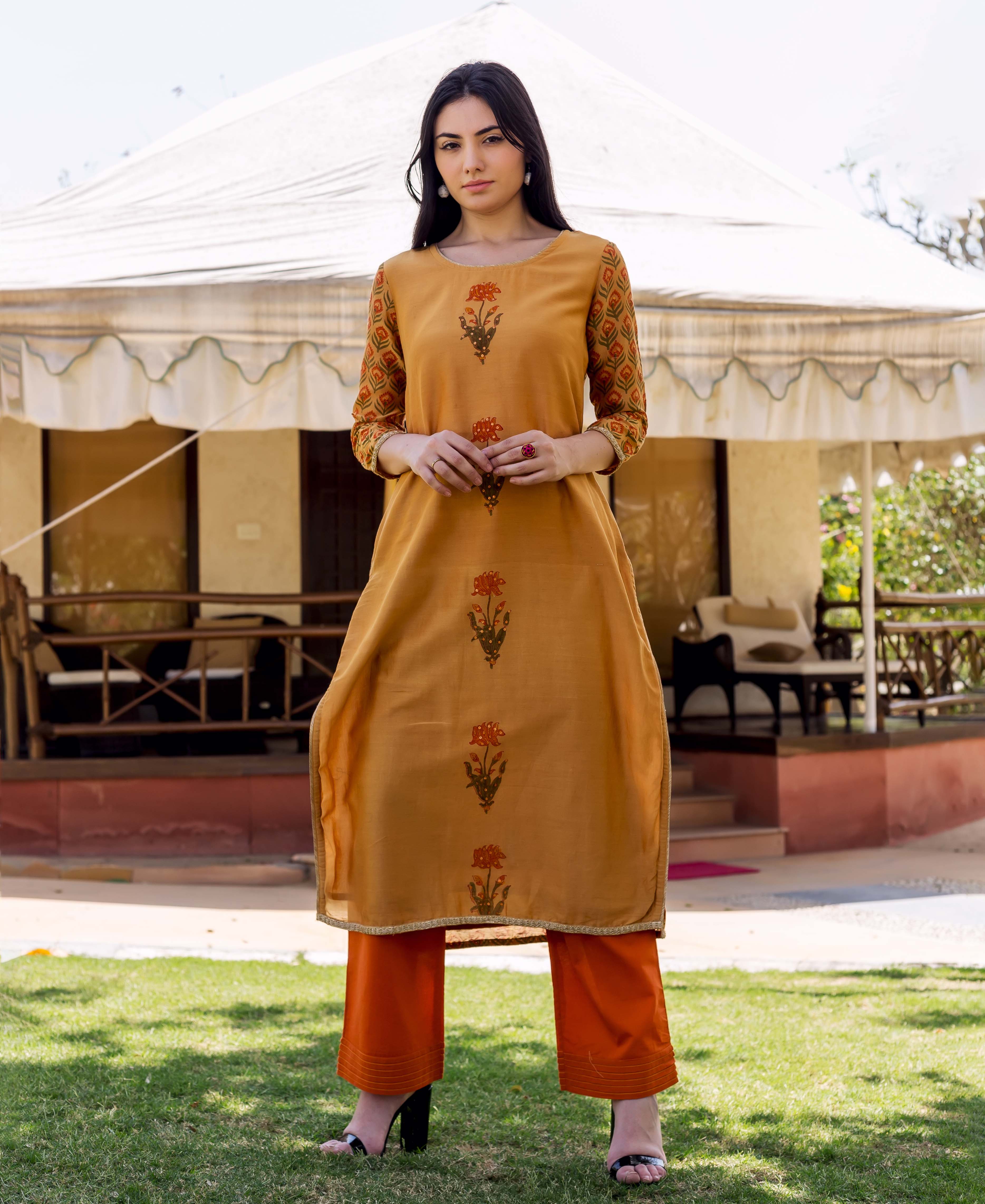 Woman wearing golden yellow Shika Block Printed Kurta with floral embroidery and orange trousers.