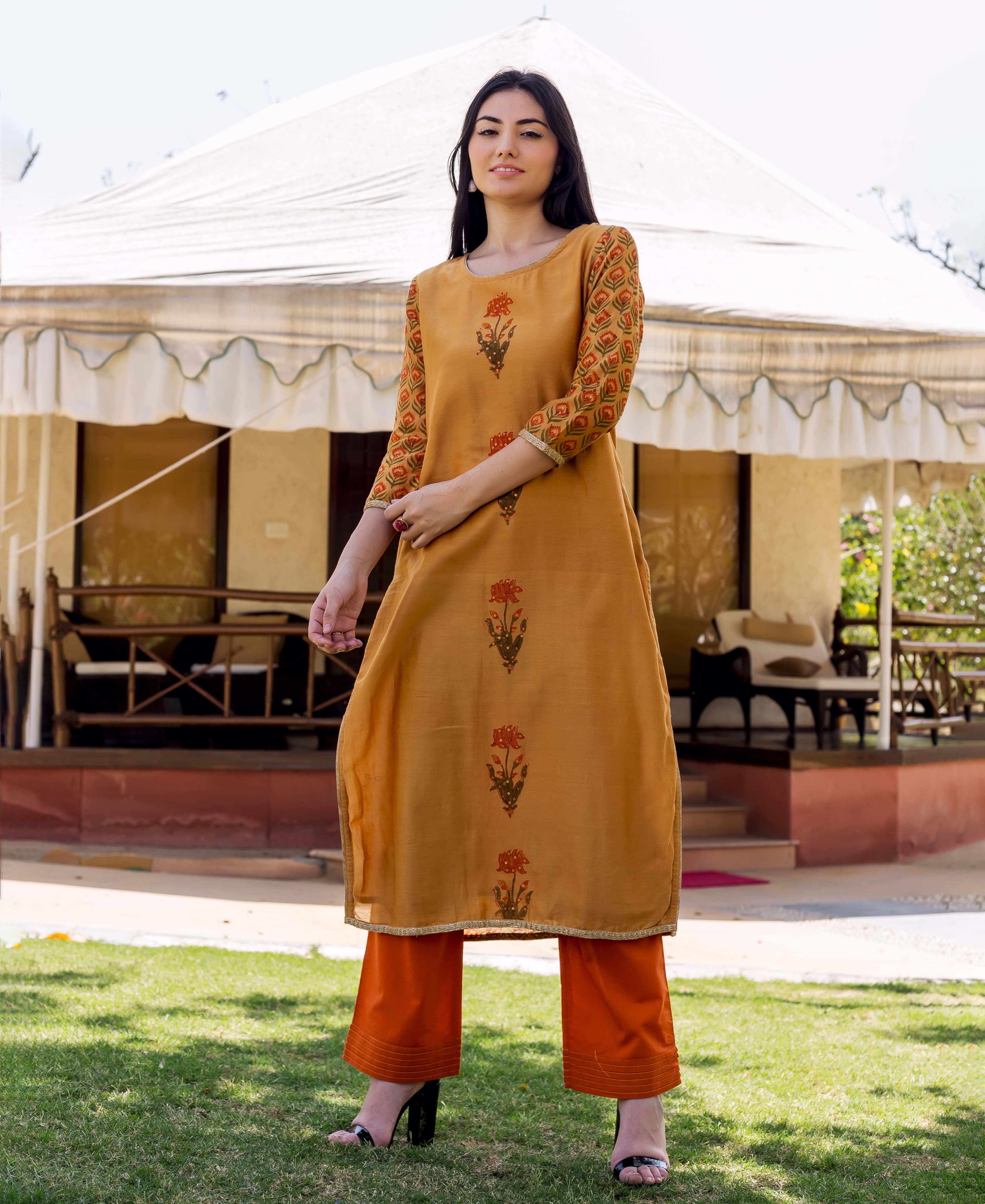 Model wears mustard yellow block-printed floral kurta with patterned sleeves and bright orange pants.