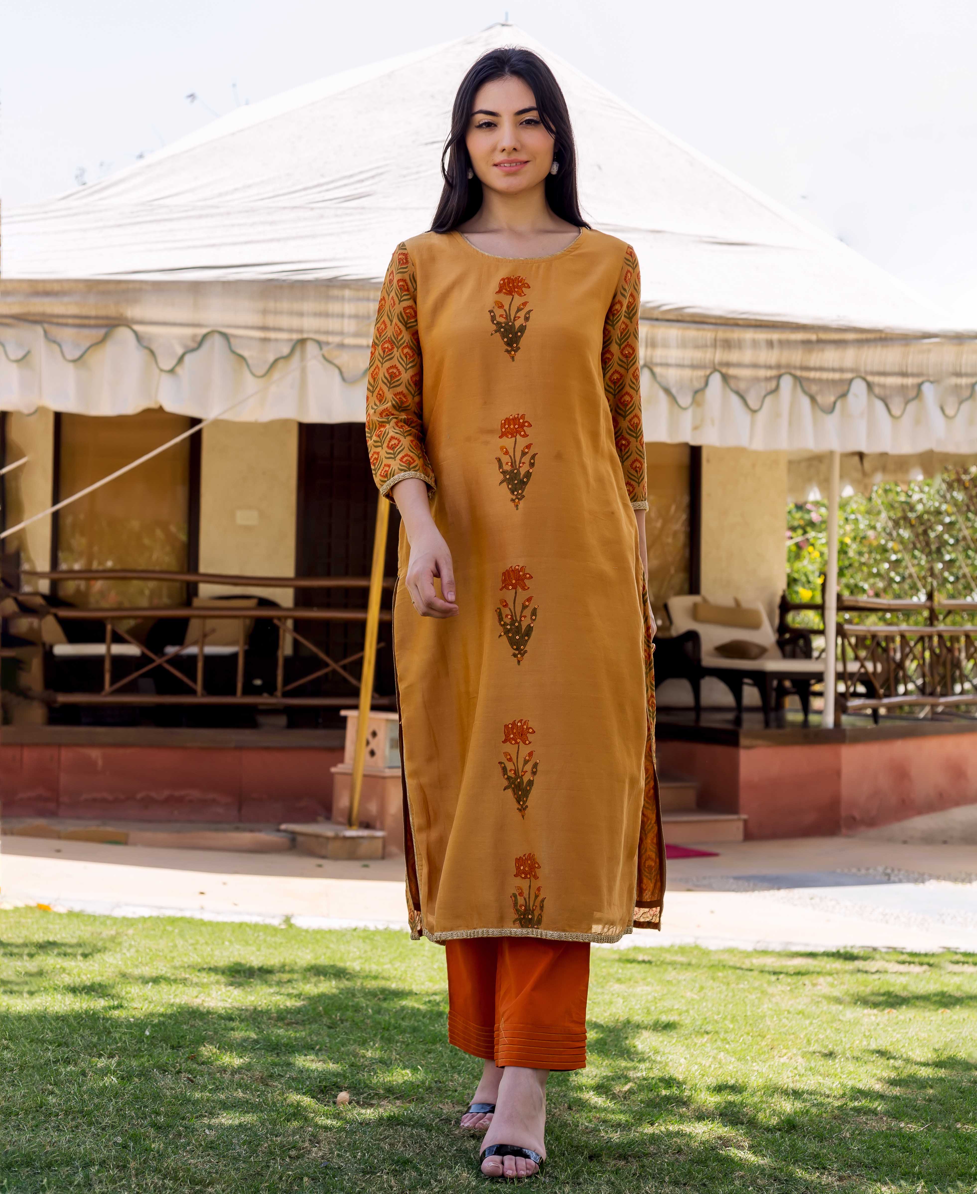 Model in mustard yellow block-printed kurta with orange floral pattern and patterned sleeves, orange pants.