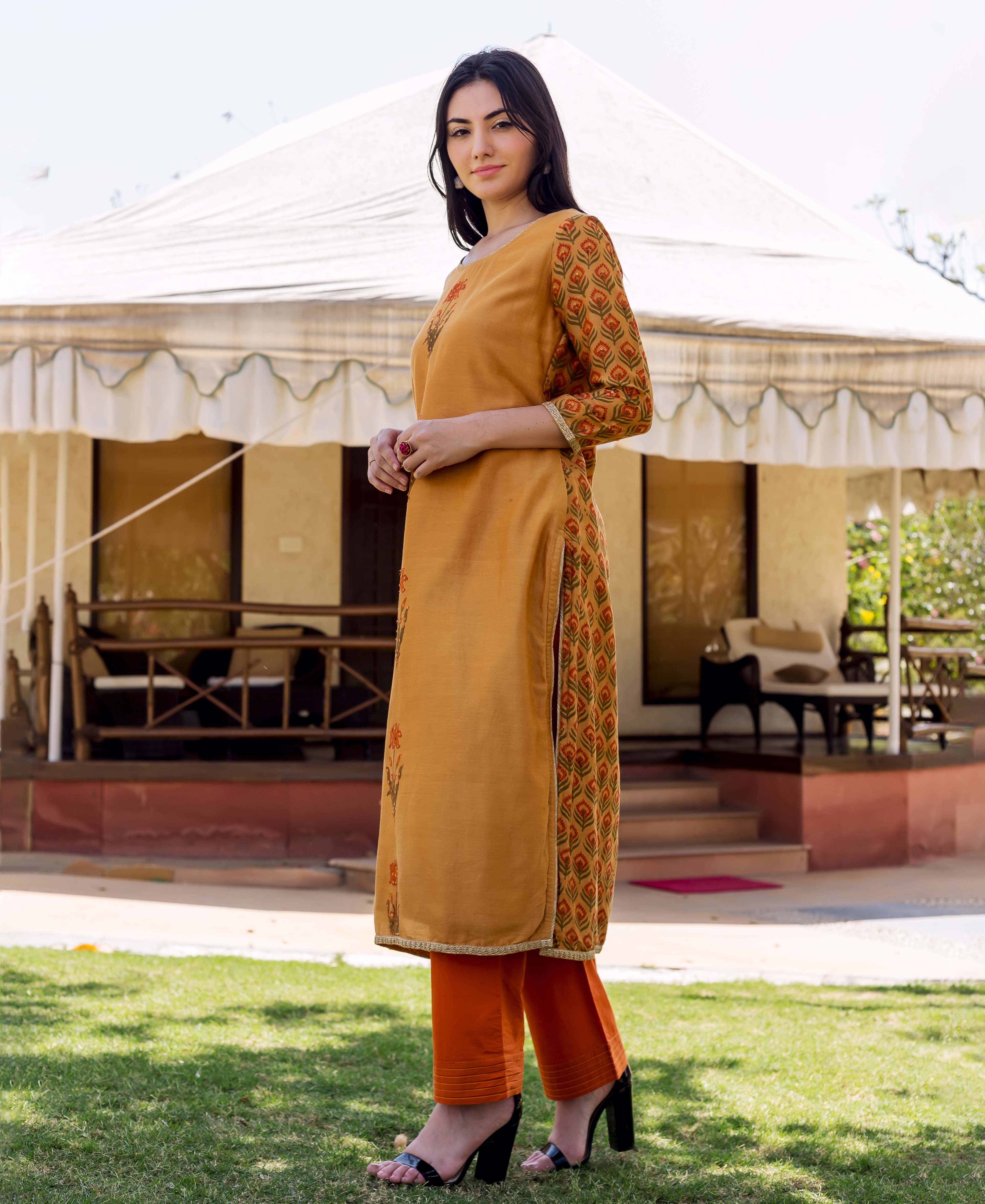 Side view of model wearing a mustard block printed and embroidered kurta with orange pants.