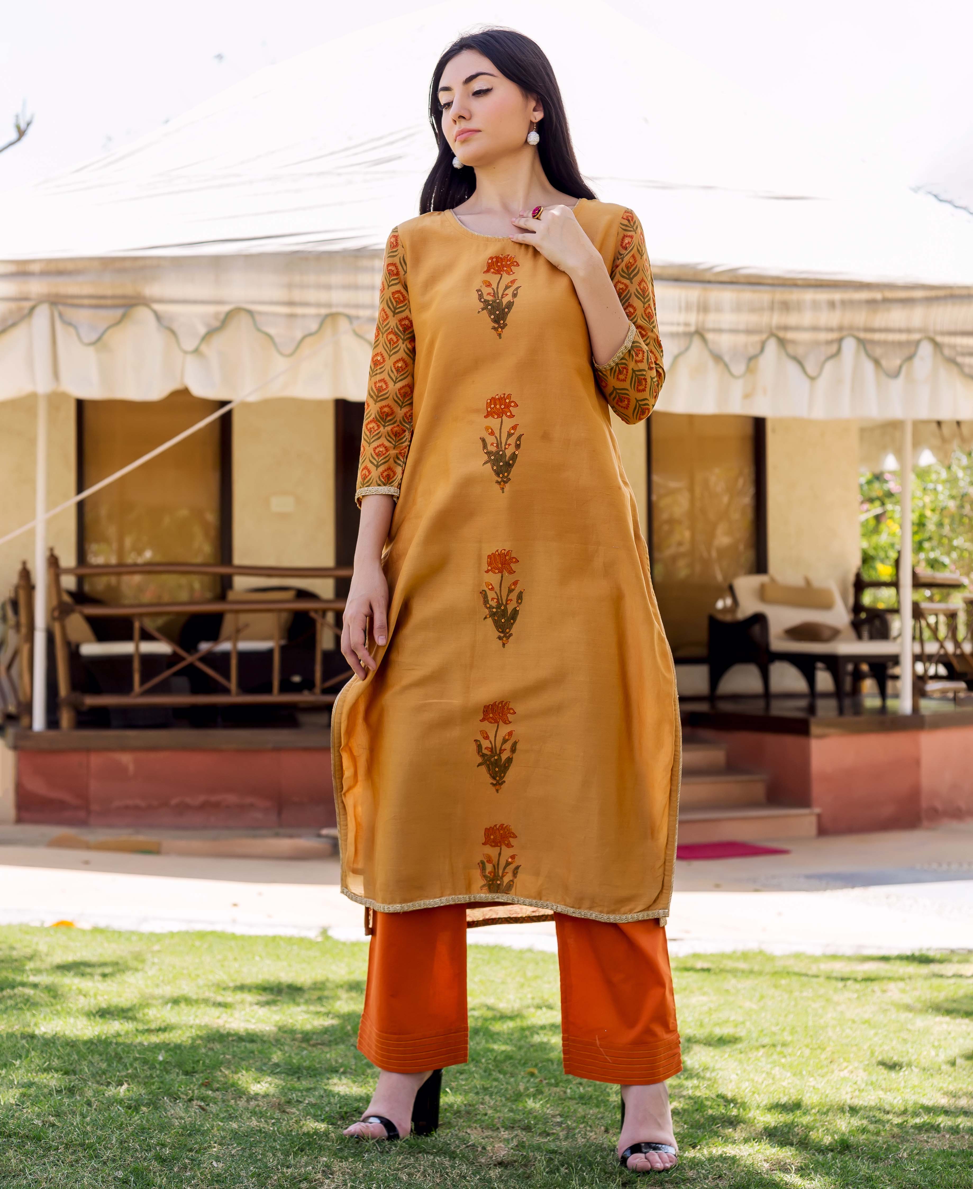 Model in a mustard block-printed kurta with floral motifs and patterned sleeves, matching orange pants.
